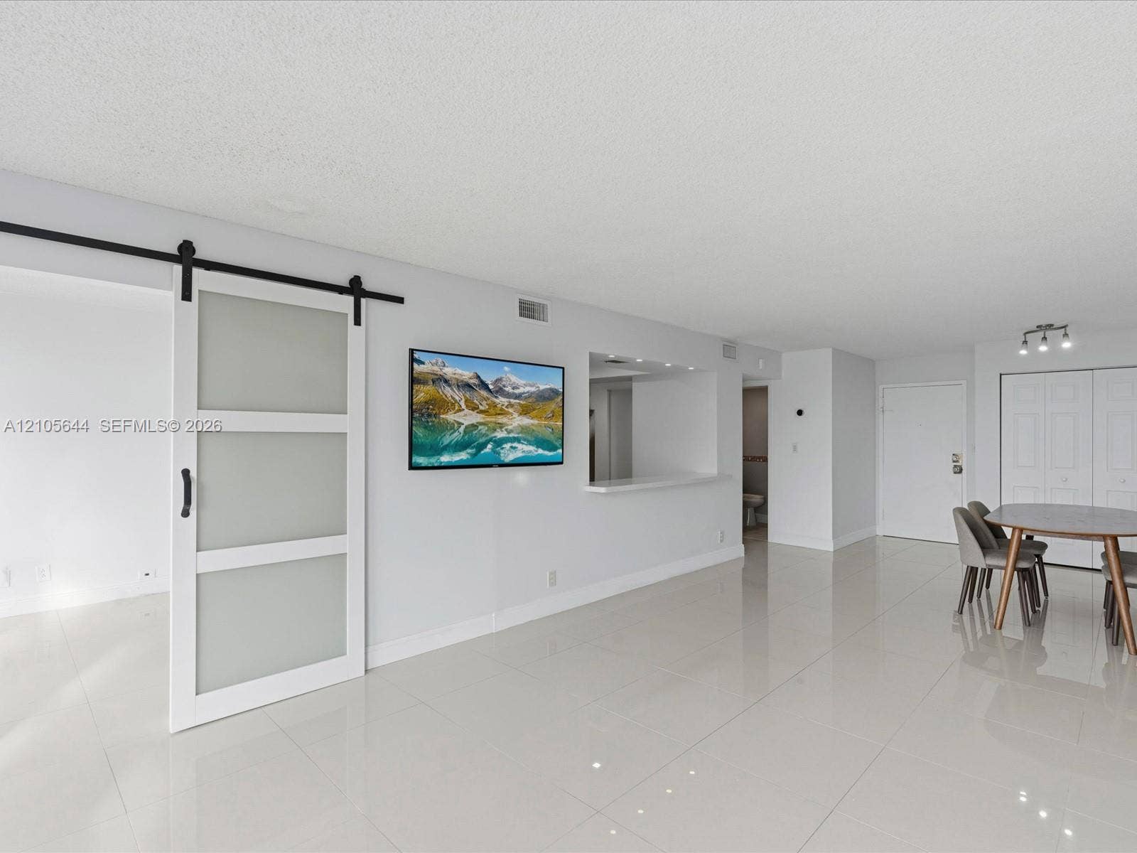 2101 Atlantic Shores Boulevard, #502, Hallandale Beach, Hallandale Beach, FL 33009 Open interior space featuring large-format tile flooring, a sliding barn-style door with frosted glass panels, a passthrough window with a ledge, and recessed lighting