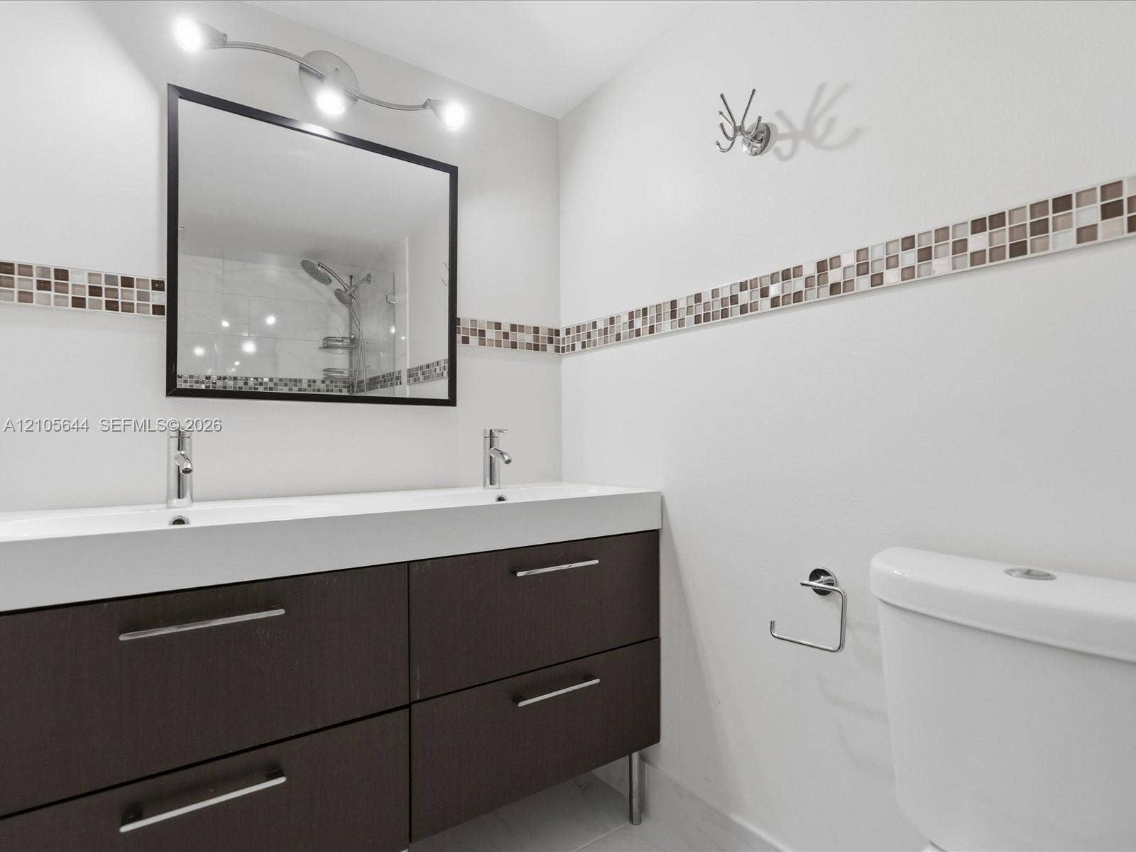 2101 Atlantic Shores Boulevard, #502, Hallandale Beach, Hallandale Beach, FL 33009 Double vanity featuring a dark-toned cabinet base with metallic hardware, integrated dual sinks, a framed mirror, and decorative mosaic tile backsplash