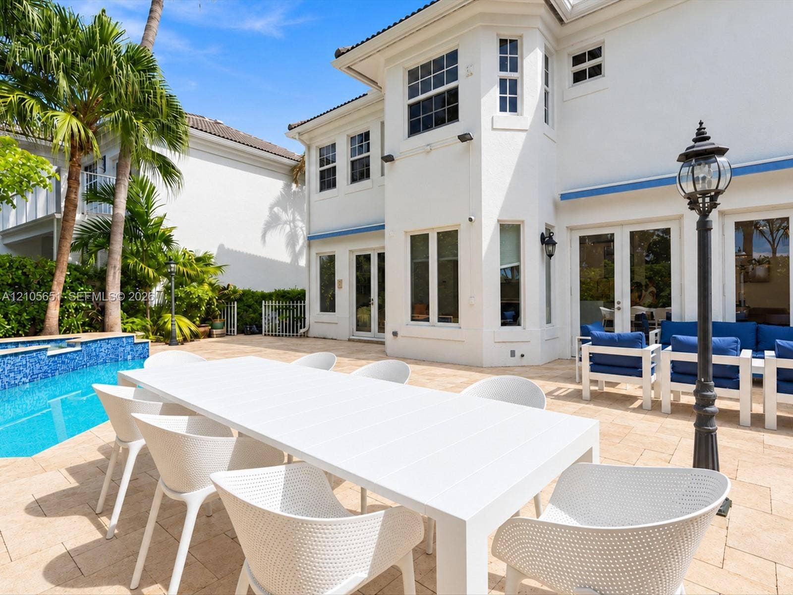Outdoor patio featuring paver flooring, a swimming pool with tile finish, multiple sets of glass-paneled double doors, and a decorative post lamp