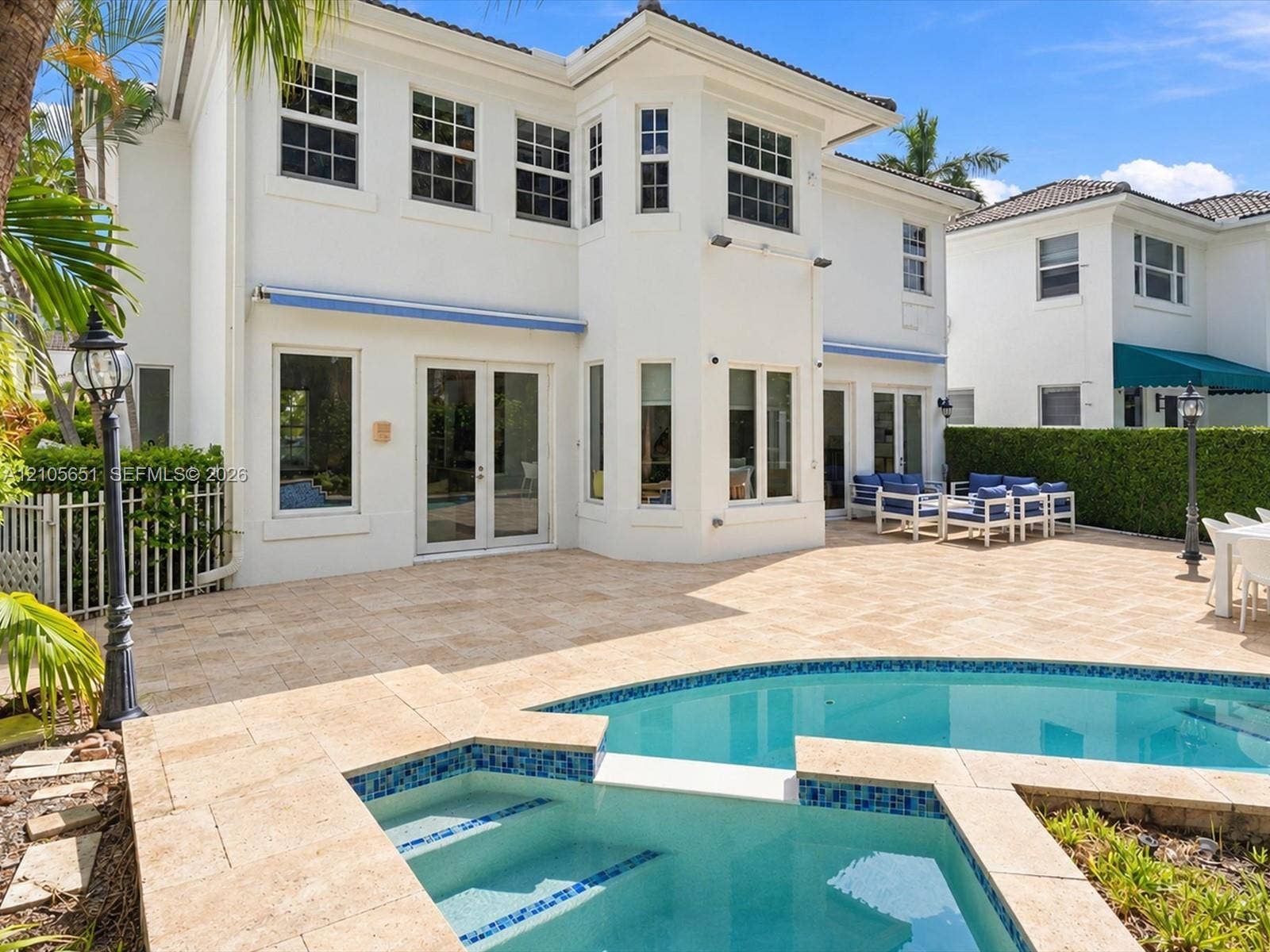 Two-story stucco exterior featuring a stone-paved patio, custom swimming pool with integrated spa, multi-pane windows, and French door entryways