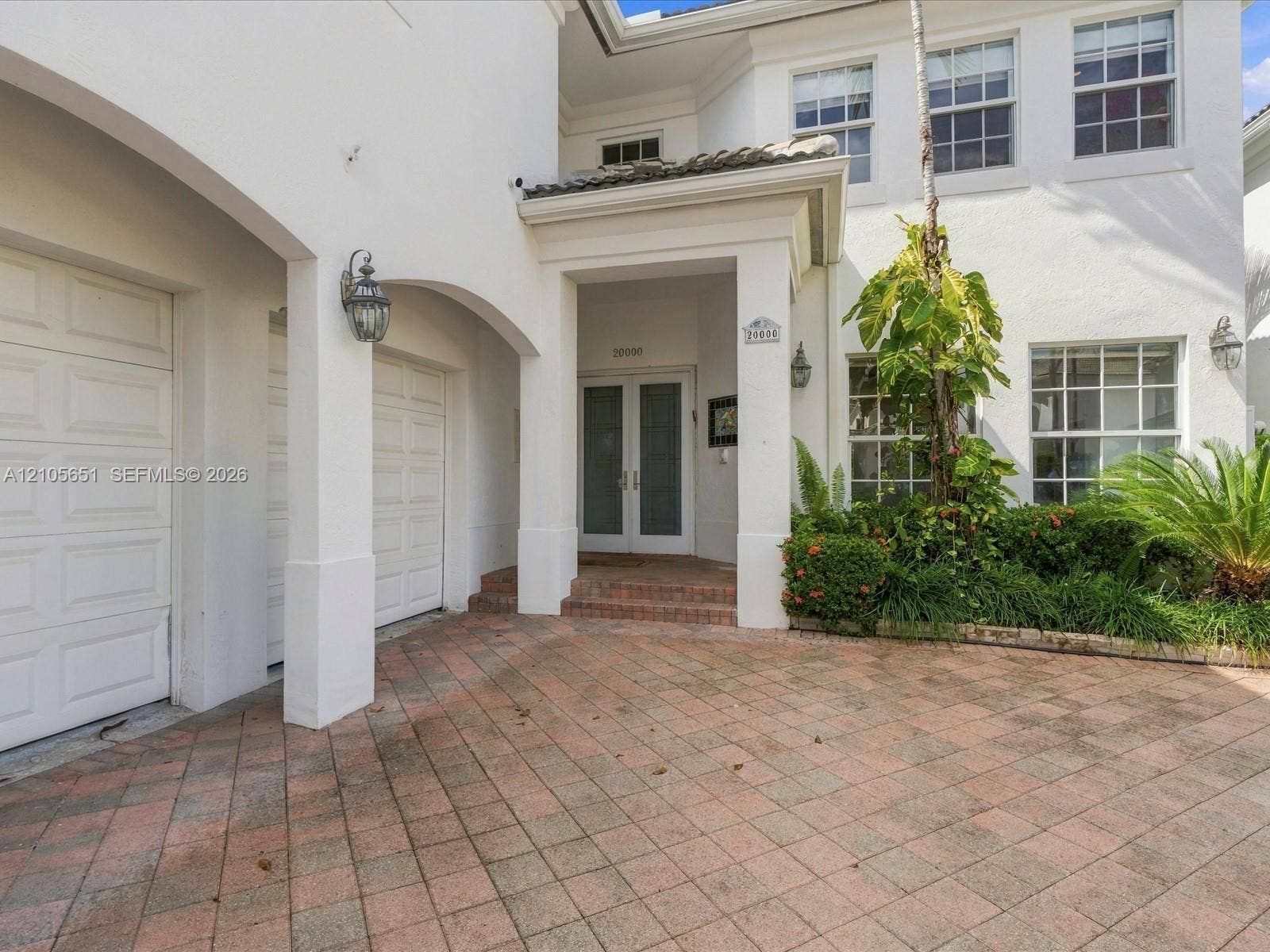 Stucco exterior featuring a covered entryway, dual-garage configuration, multi-pane windows, and a paved stone driveway