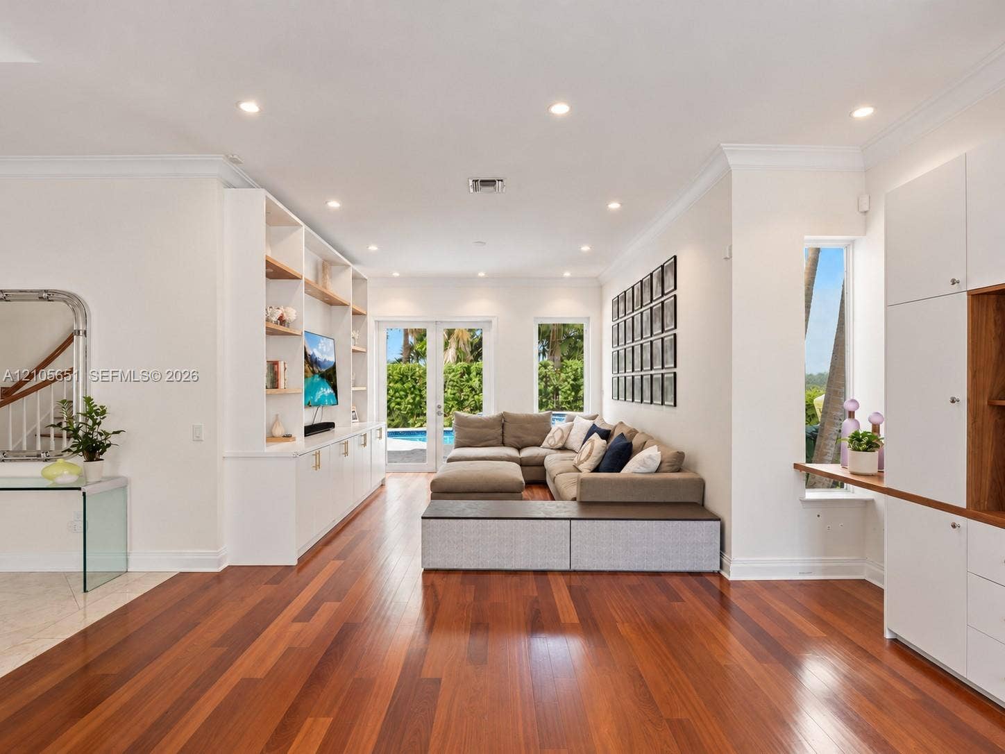 Living area featuring wood-finish flooring, recessed lighting, floor-to-ceiling custom built-in cabinetry, and French doors