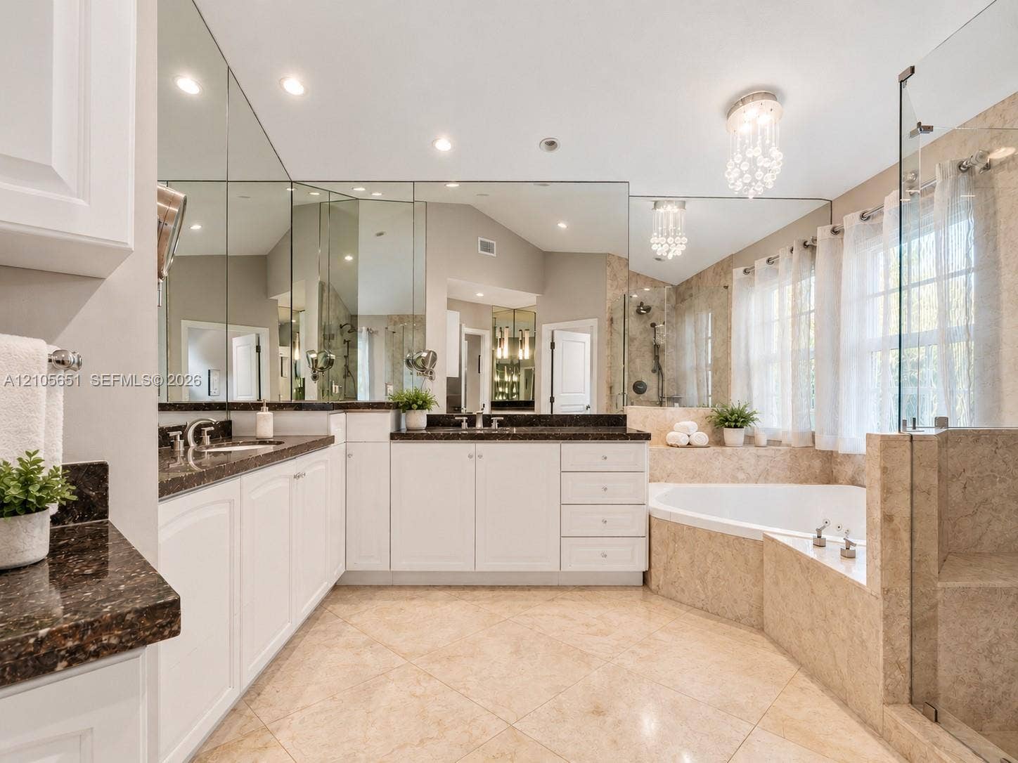 Bathroom featuring a double vanity with stone countertops, tiled soaking tub, walk-in glass-enclosed shower, wall-to-wall mirrors, and crystal light fixtures