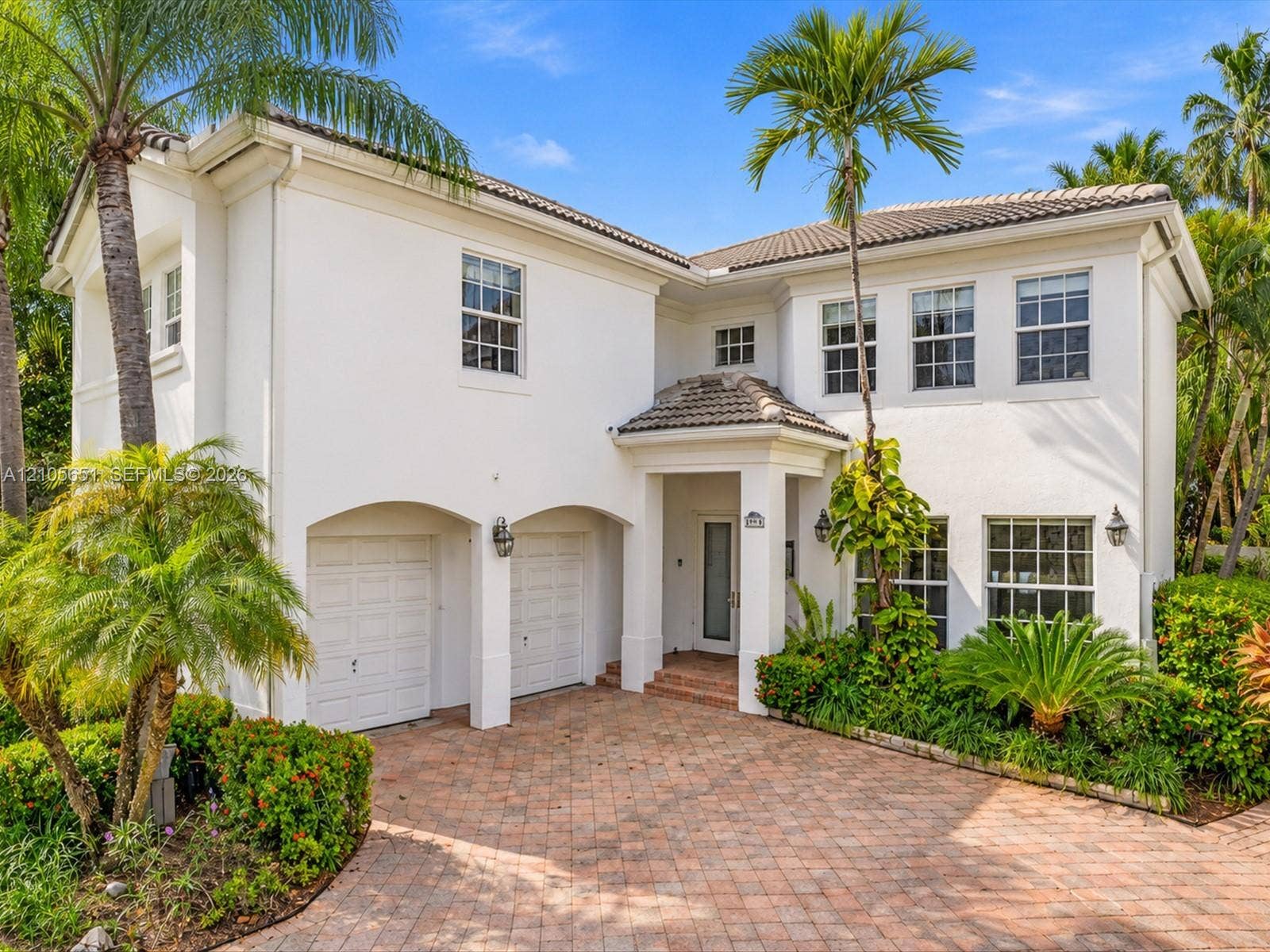 Two-story stucco exterior featuring a covered entryway, multi-pane windows, a tiled roof, and a paved brick driveway with an integrated two-car garage