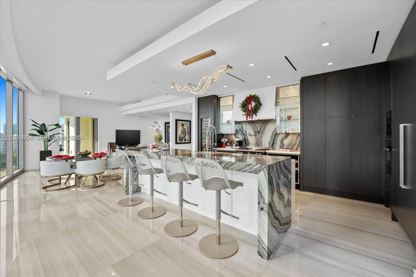 Open-concept kitchen featuring a waterfall-edge stone island, high-gloss flat-panel cabinetry, floor-to-ceiling dark cabinetry, large-format tile flooring, and custom contemporary lighting