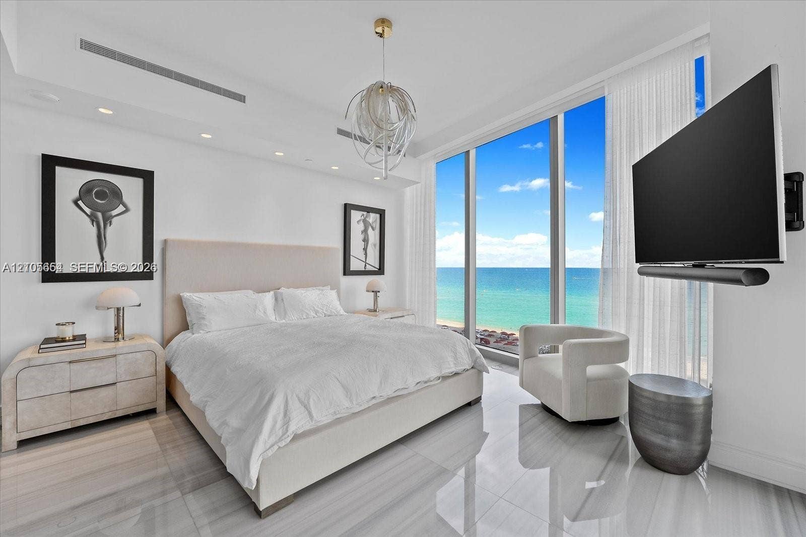 Floor-to-ceiling windows featuring ocean panoramas, polished stone flooring, recessed ceiling lighting, and a contemporary spherical chandelier