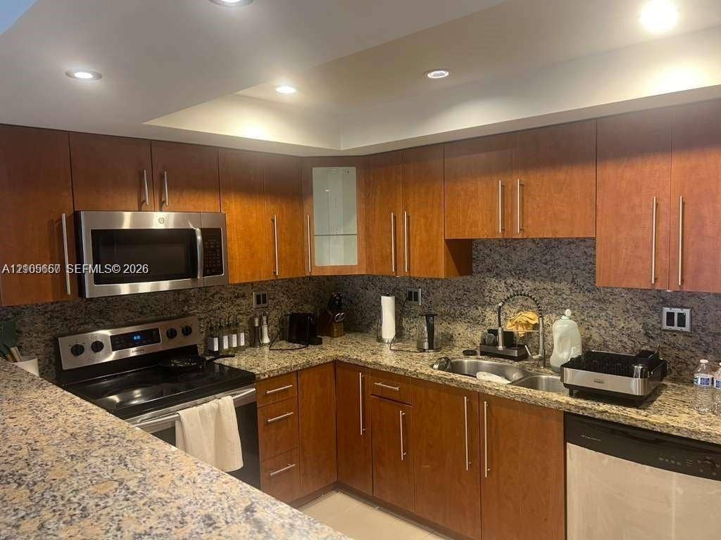 19380 Collins Avenue, #808, Sunny Isles Beach, FL 33160 Kitchen featuring wood cabinetry, stone countertops, stainless steel microwave, recessed lighting, and a dual-basin sink with a gooseneck faucet