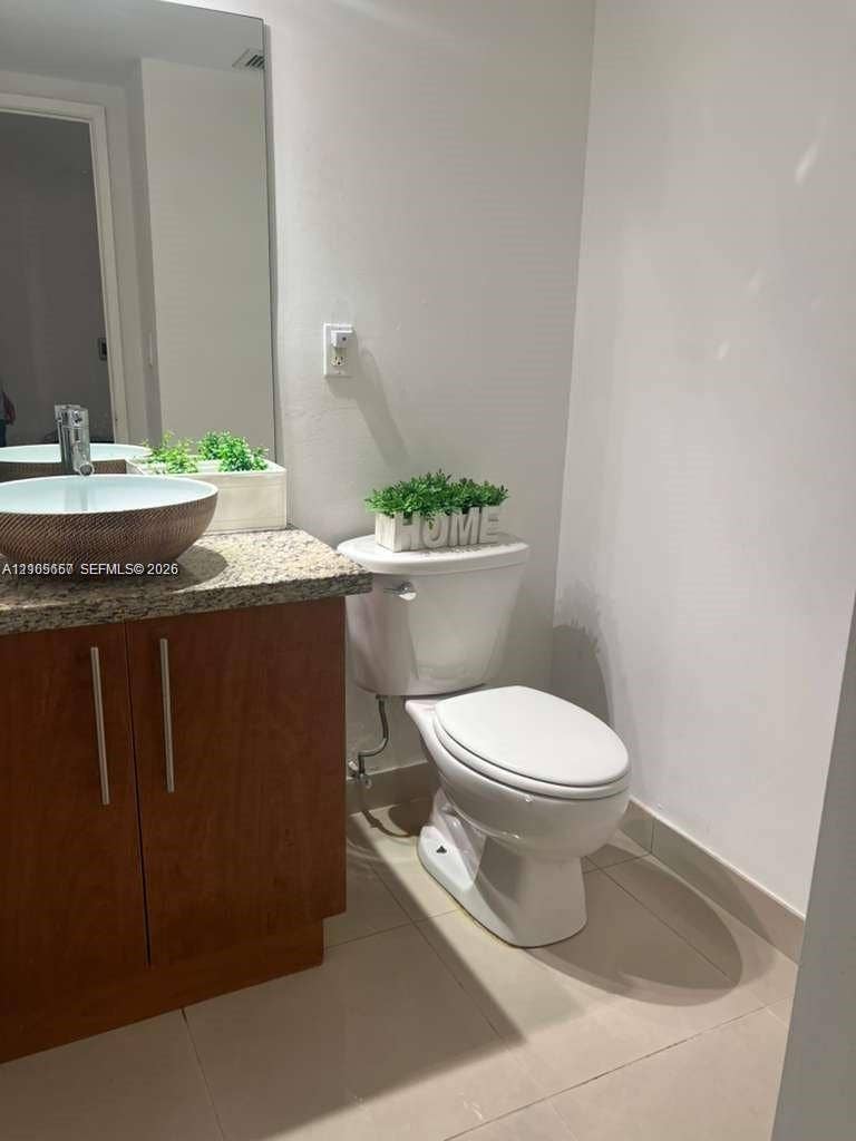 19380 Collins Avenue, #808, Sunny Isles Beach, FL 33160 Wood-finish cabinetry, stone-texture countertop, vessel sink with metal faucet, large wall-mounted mirror, and tile flooring