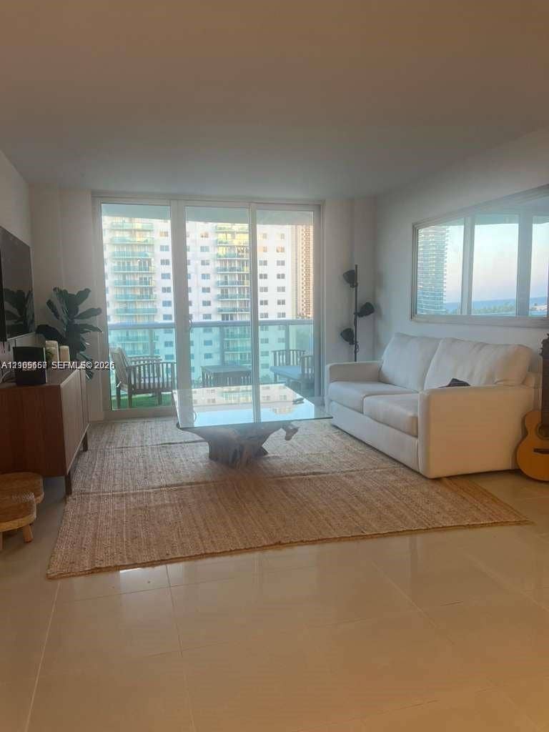 19380 Collins Avenue, #808, Sunny Isles Beach, FL 33160 Living area featuring expansive floor-to-ceiling glass doors, neutral tile flooring, and a private balcony