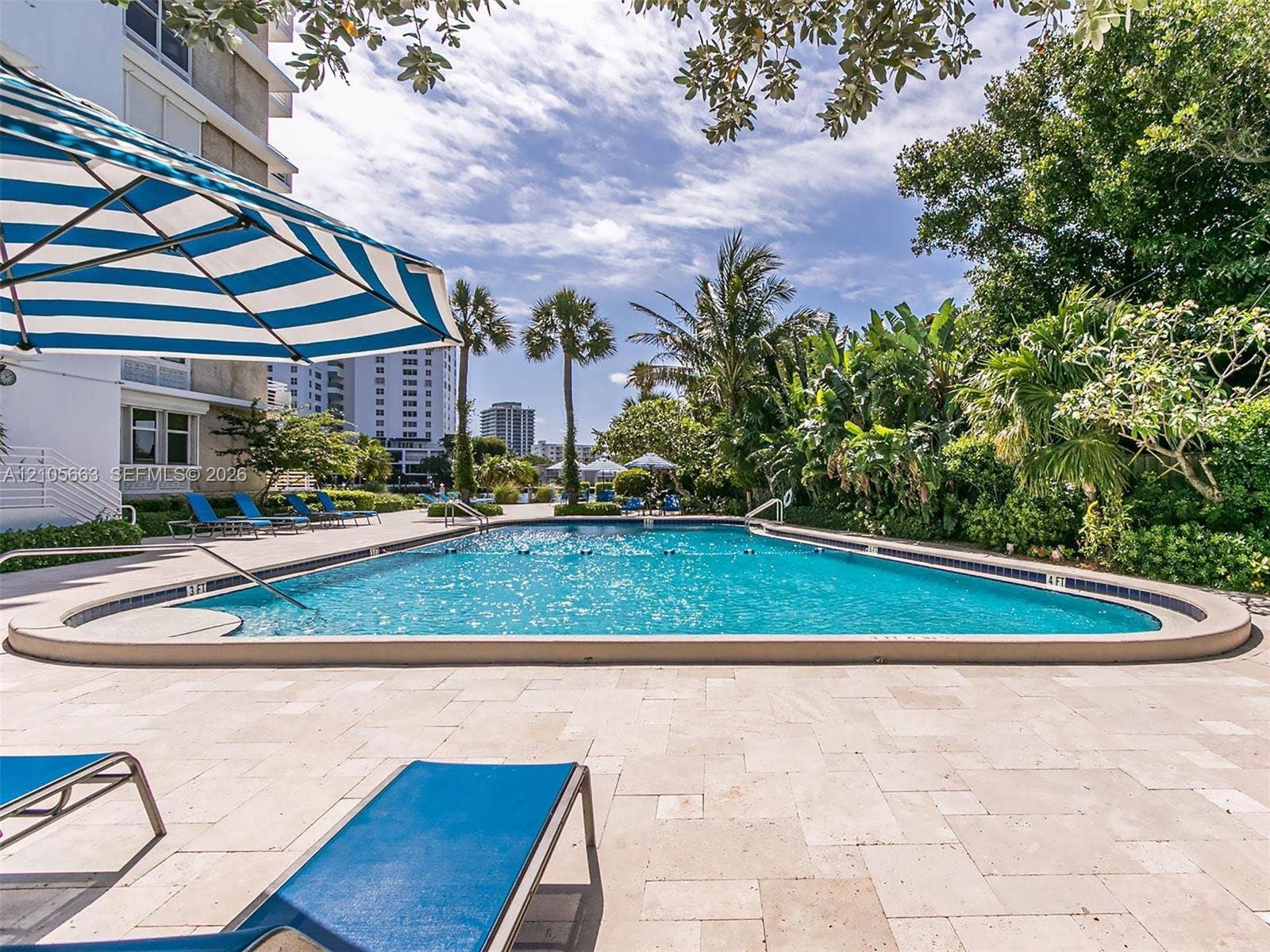 In-ground swimming pool featuring stone-paver decking, metal handrails, and mature tropical landscaping