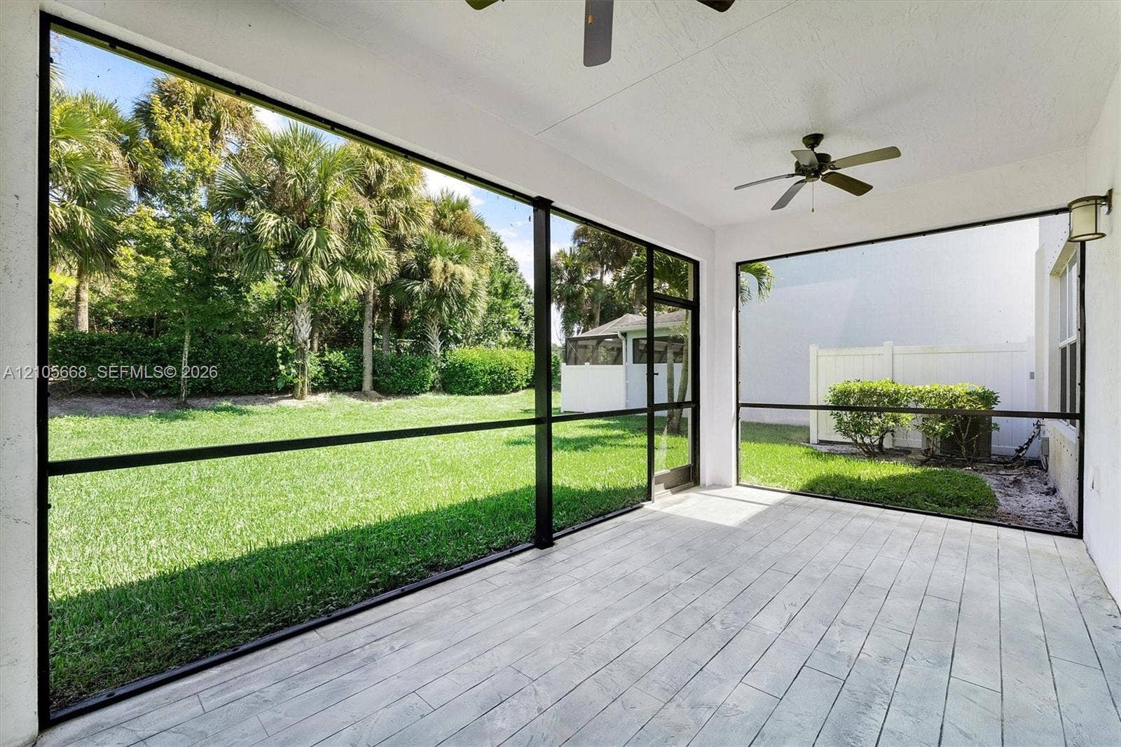 6307 Trails Of Foxford Court, West Palm Beach, FL 33415 Screened-in patio featuring wood-finish flooring, two ceiling fans, wall-mounted exterior lighting, and a fenced yard with mature landscaping