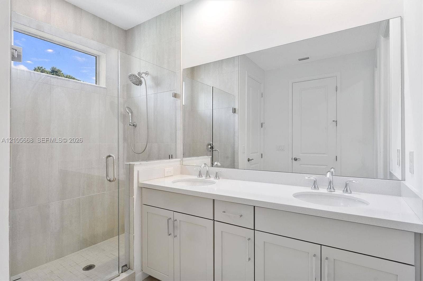 6307 Trails Of Foxford Court, West Palm Beach, FL 33415 Double vanity featuring white cabinetry, solid surface countertops, dual undermount sinks, and a full-width wall mirror, alongside a glass-enclosed shower with tile surround and adjustable handheld shower head