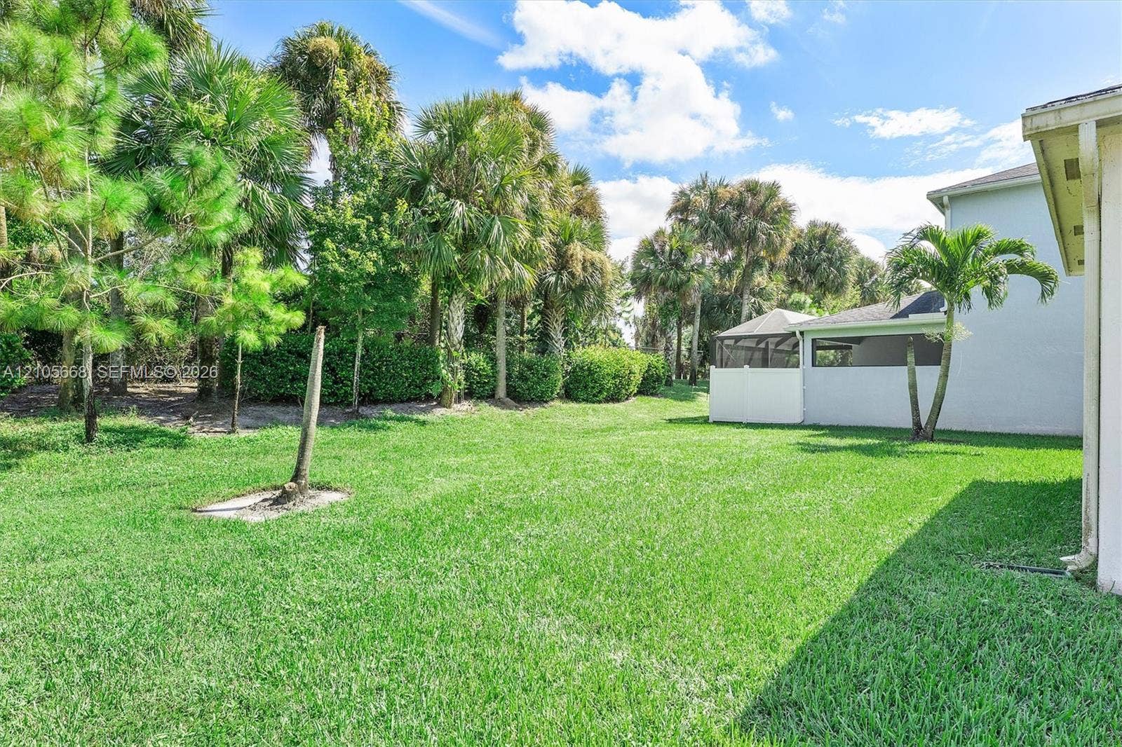 6307 Trails Of Foxford Court, West Palm Beach, FL 33415 Expansive backyard featuring a level lawn, mature palm trees, dense perimeter landscaping, and a screened-in rear patio enclosure