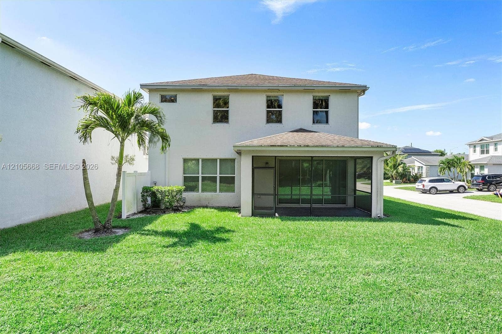 6307 Trails Of Foxford Court, West Palm Beach, FL 33415 Two-story exterior featuring a stucco facade, a hip roof, a covered screened-in lanai, and a sodded lawn with palm tree landscaping
