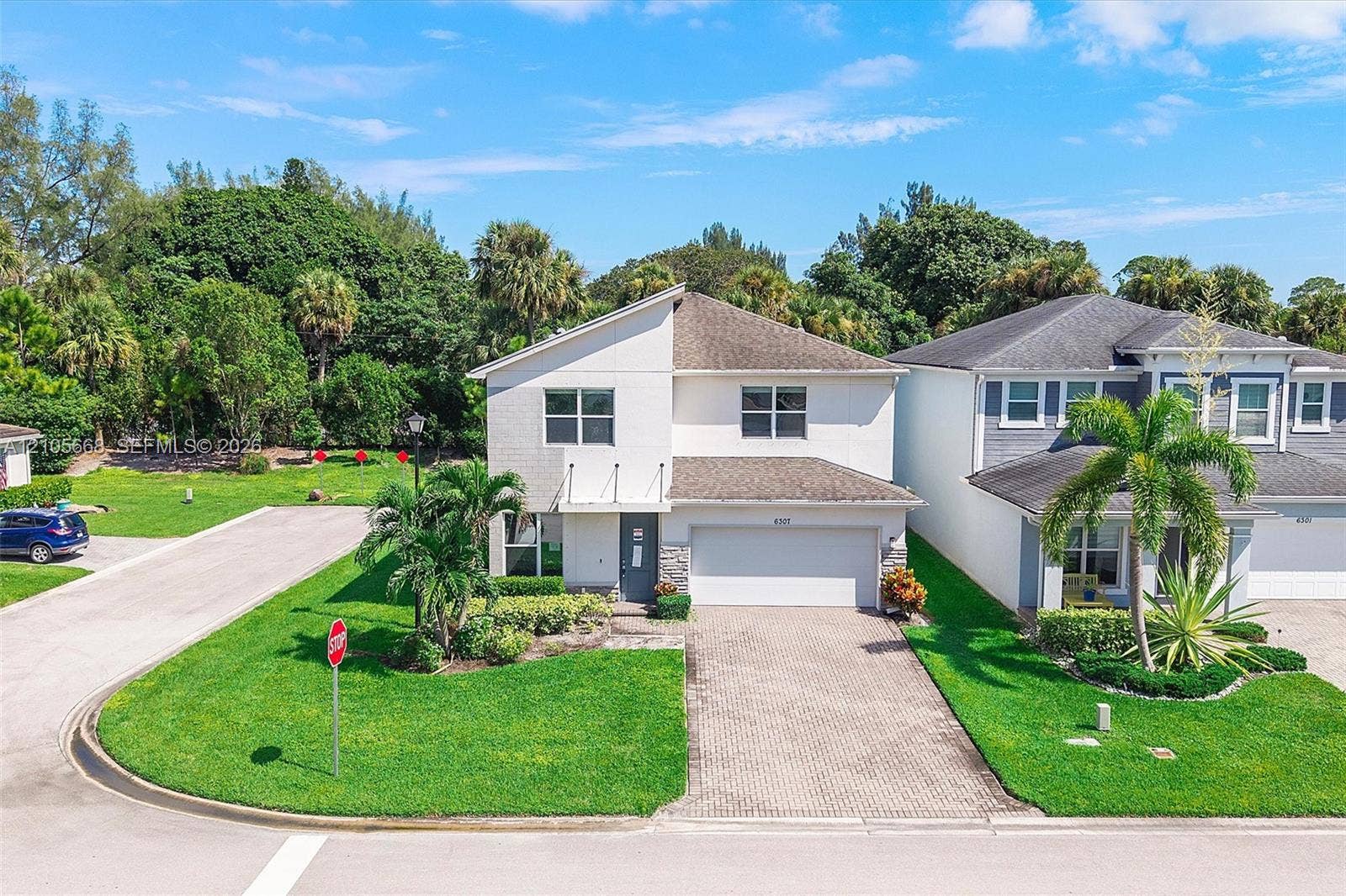 6307 Trails Of Foxford Court, West Palm Beach, FL 33415 Two-story residence featuring a combination of smooth stucco and stone-finish siding, a multi-car paved driveway, an attached garage, and a manicured lawn with tropical landscaping