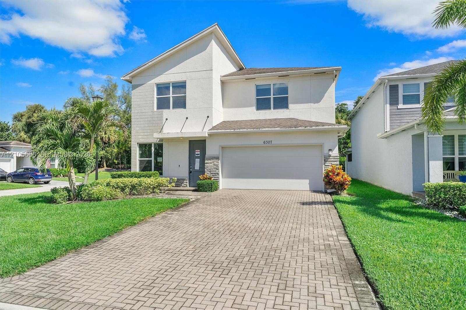 6307 Trails Of Foxford Court, West Palm Beach, FL 33415 Two-story exterior featuring a light-toned stucco faade, stone veneer accents, a multi-paneled garage door, and a herringbone-patterned paved driveway
