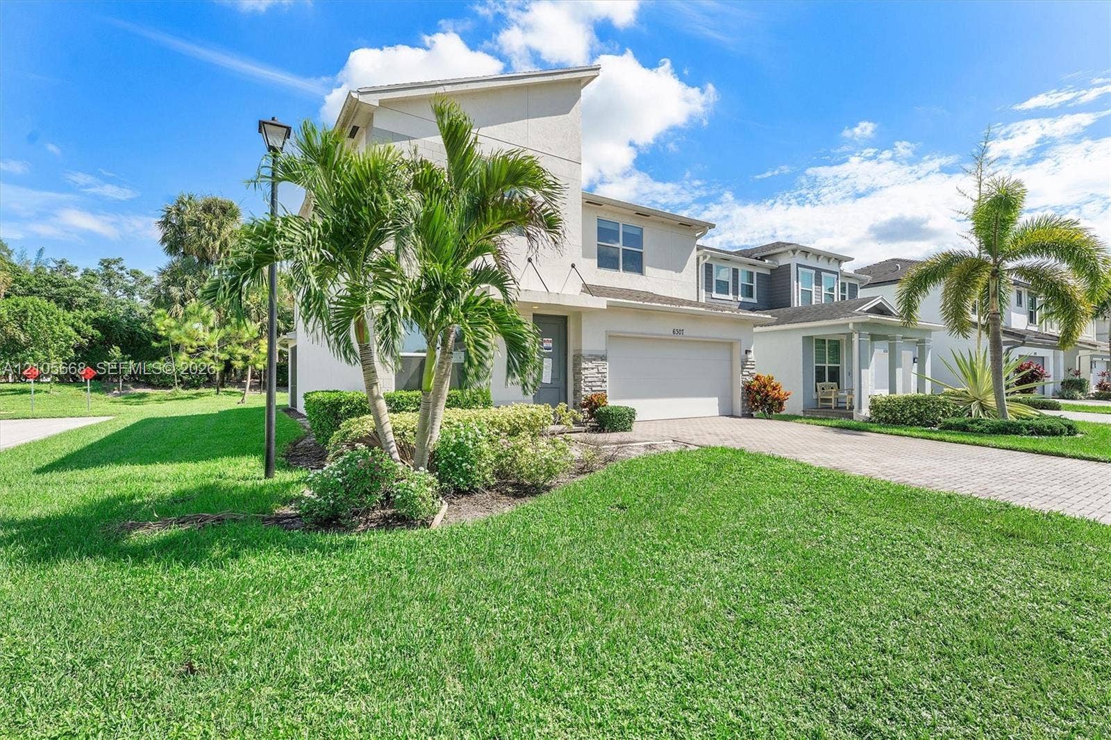 6307 Trails Of Foxford Court, West Palm Beach, FL 33415 Two-story stucco exterior with stone veneer accents, multi-level roofline, paver driveway, attached garage, and landscaped front yard with palm trees