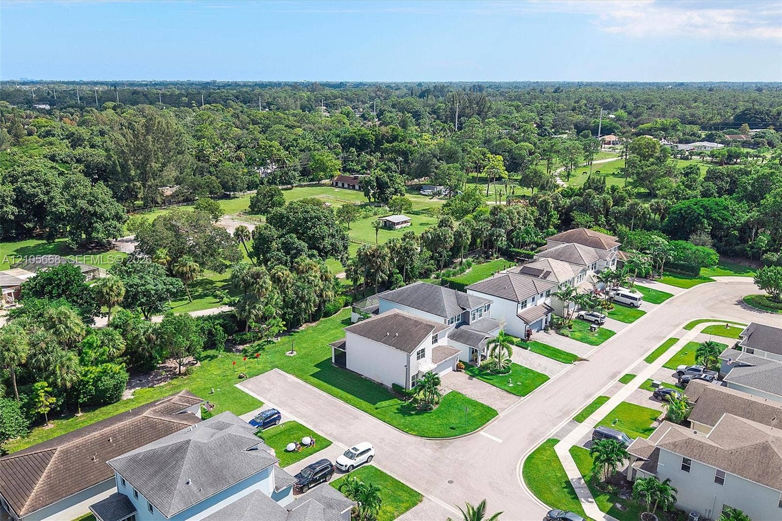 6307 Trails Of Foxford Court, West Palm Beach, FL 33415 Aerial view featuring residential properties with shingled roofs, integrated multi-car garages, manicured lawns, and expansive surrounding green space with mature trees