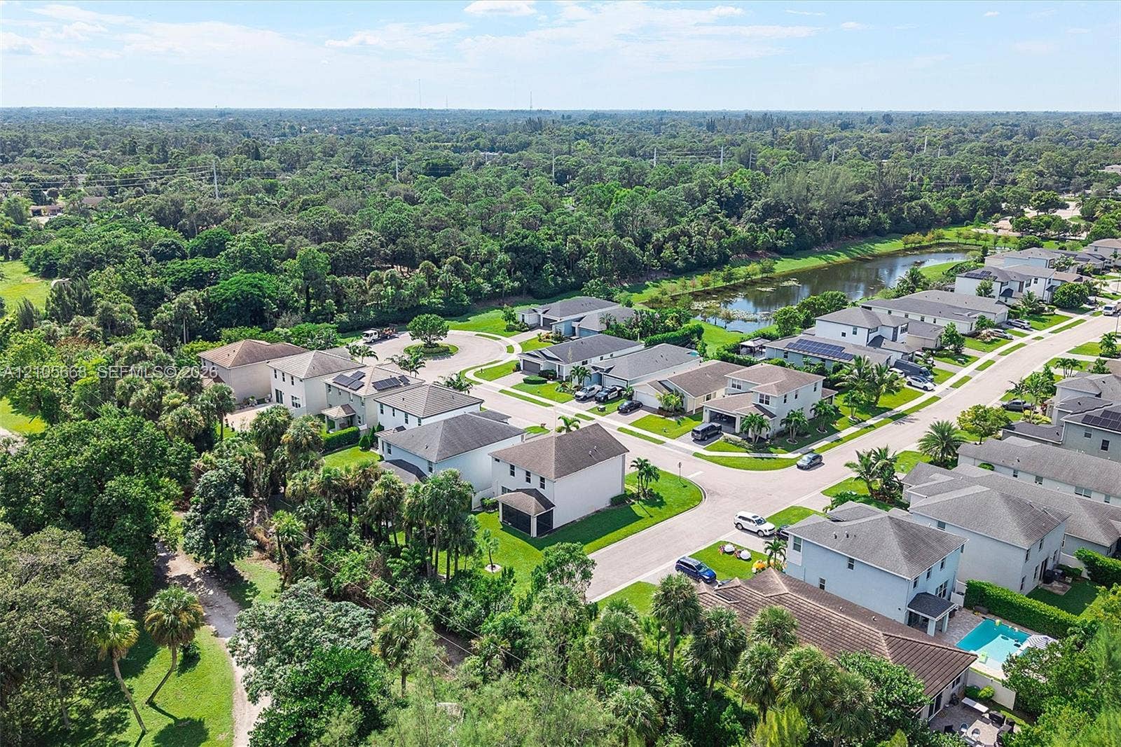 6307 Trails Of Foxford Court, West Palm Beach, FL 33415 Aerial perspective of a suburban neighborhood featuring multi-story residential structures, integrated paved roadways, mature wooded canopy, and a central retention pond