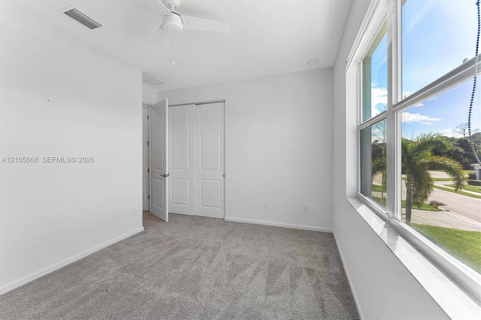 6307 Trails Of Foxford Court, West Palm Beach, FL 33415 Neutral-toned carpeting, large windows, white paneled closet doors, and a ceiling-mounted fan