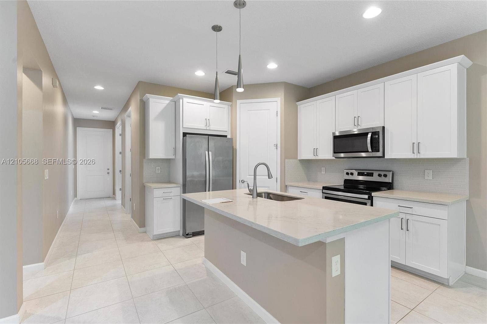 6307 Trails Of Foxford Court, West Palm Beach, FL 33415 Kitchen featuring white shaker-style cabinetry, a central island with a stainless steel sink, light-toned stone-finish countertops, stainless steel appliances, and pendant lighting