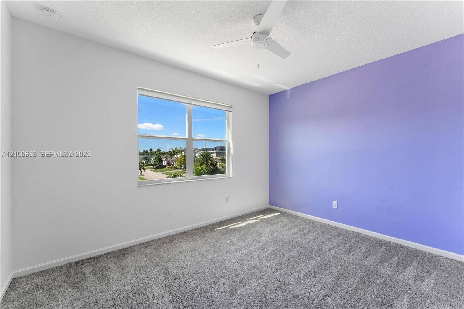 6307 Trails Of Foxford Court, West Palm Beach, FL 33415 Neutral-toned wall interior featuring a vibrant accent wall, gray carpeting, a multi-blade ceiling fan, and a single-pane window