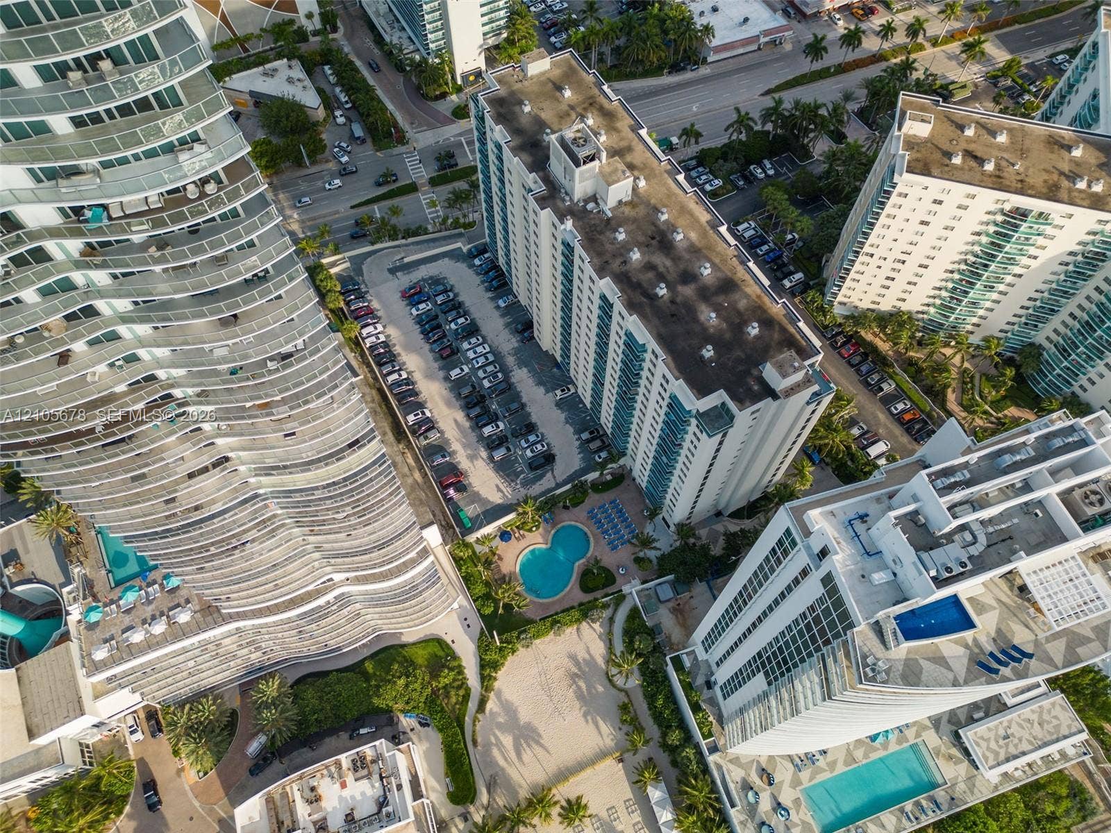 4001 S Ocean Drive, #14F, Hollywood, FL 33019 Aerial view showcasing a contemporary residential complex featuring multiple curved-facade towers with balconies, resort-style amenities including swimming pools, manicured landscaping with mature trees, and integrated parking structures