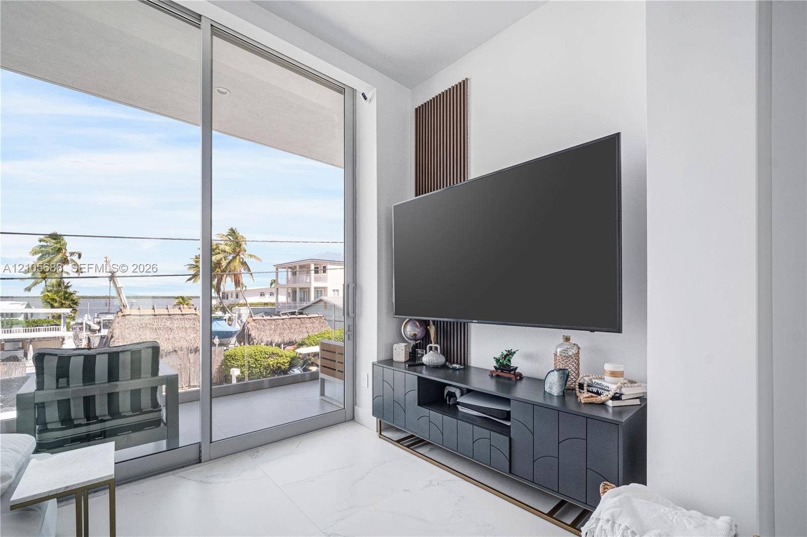 164 W Avenue C, Key Largo, FL 33037 Floor-to-ceiling sliding glass doors, white stone-finish tile flooring, and a decorative vertical slat wood wall accent