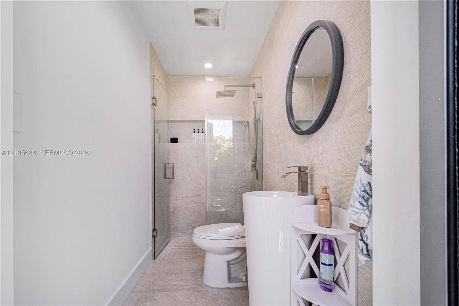 164 W Avenue C, Key Largo, FL 33037 Pedestal sink with metallic faucet, round mirror, glass-enclosed shower, and textured stone-finish wall tile
