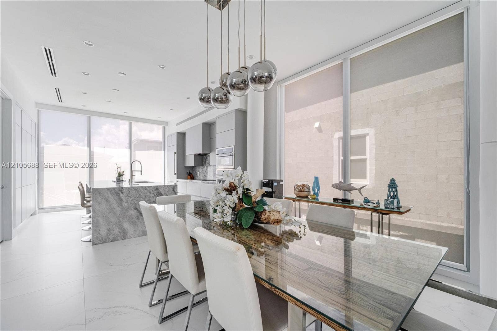 164 W Avenue C, Key Largo, FL 33037 Modern kitchen featuring a waterfall edge stone island, floor-to-ceiling glass panel walls, flat-panel cabinetry, recessed ceiling lighting, and a multi-sphere pendant light fixture