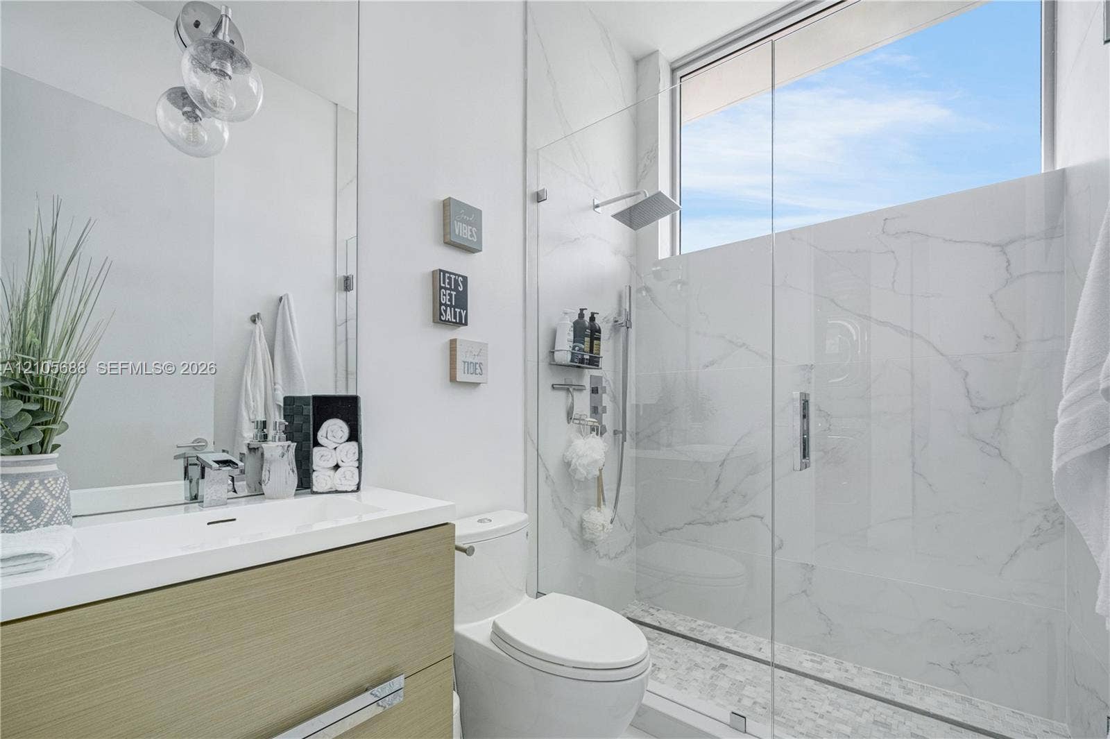 164 W Avenue C, Key Largo, FL 33037 Floating wood-finish vanity with integrated sink, full-height walk-in shower featuring large-format stone-pattern tile, frameless glass enclosure, rainfall showerhead, and upper transom window