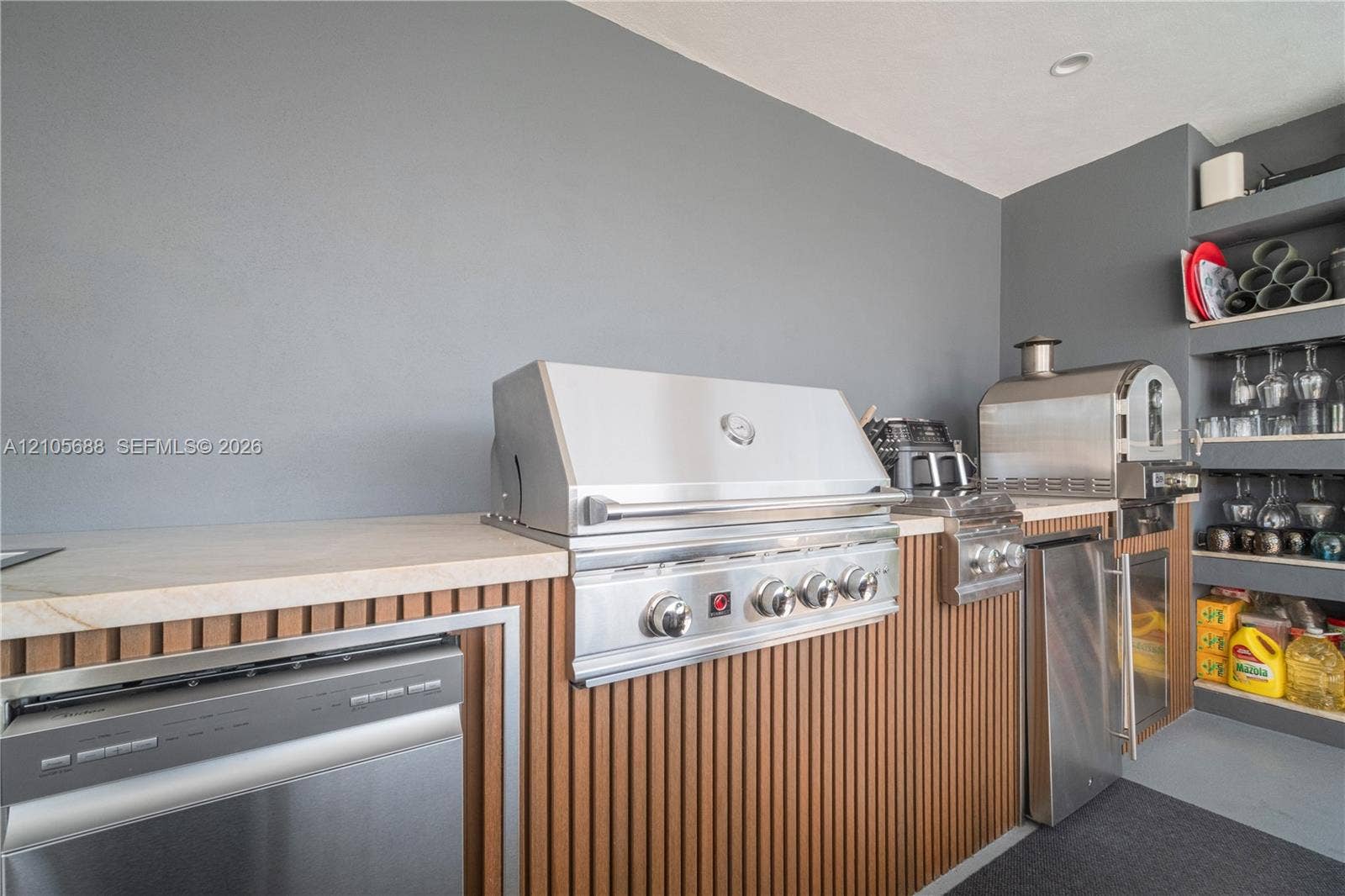 164 W Avenue C, Key Largo, FL 33037 Outdoor kitchen featuring stainless steel appliances, stone-look countertops, vertical wood-slat cabinetry, and integrated shelving