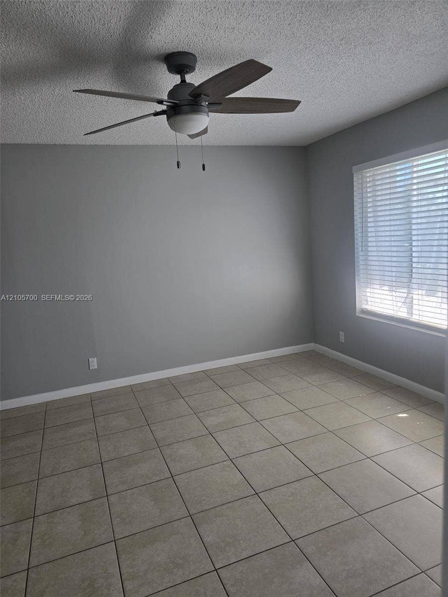 Neutral-toned wall finish, large-format tile flooring, five-blade ceiling fan with integrated lighting, and horizontal window blinds