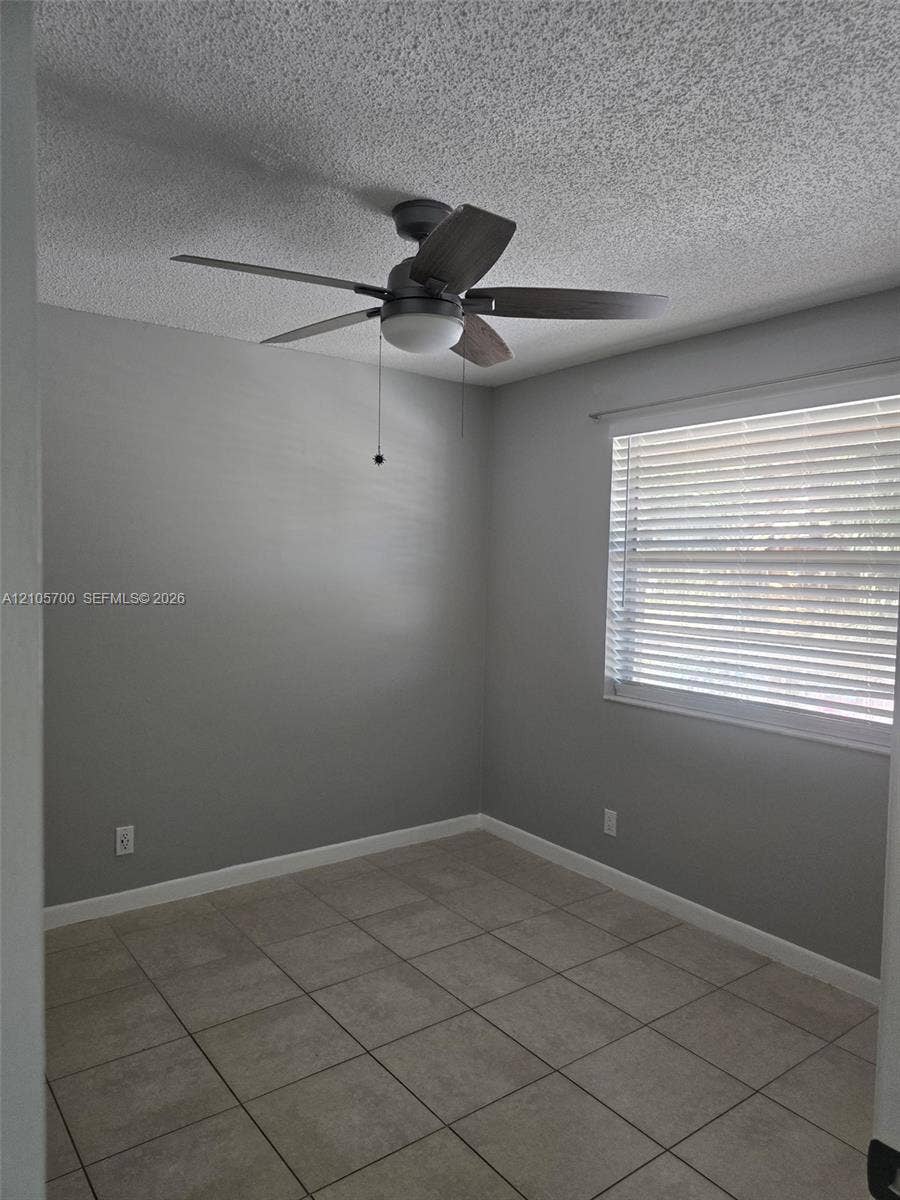 Neutral gray wall paint, ceramic tile flooring, and a ceiling fan with integrated light fixture