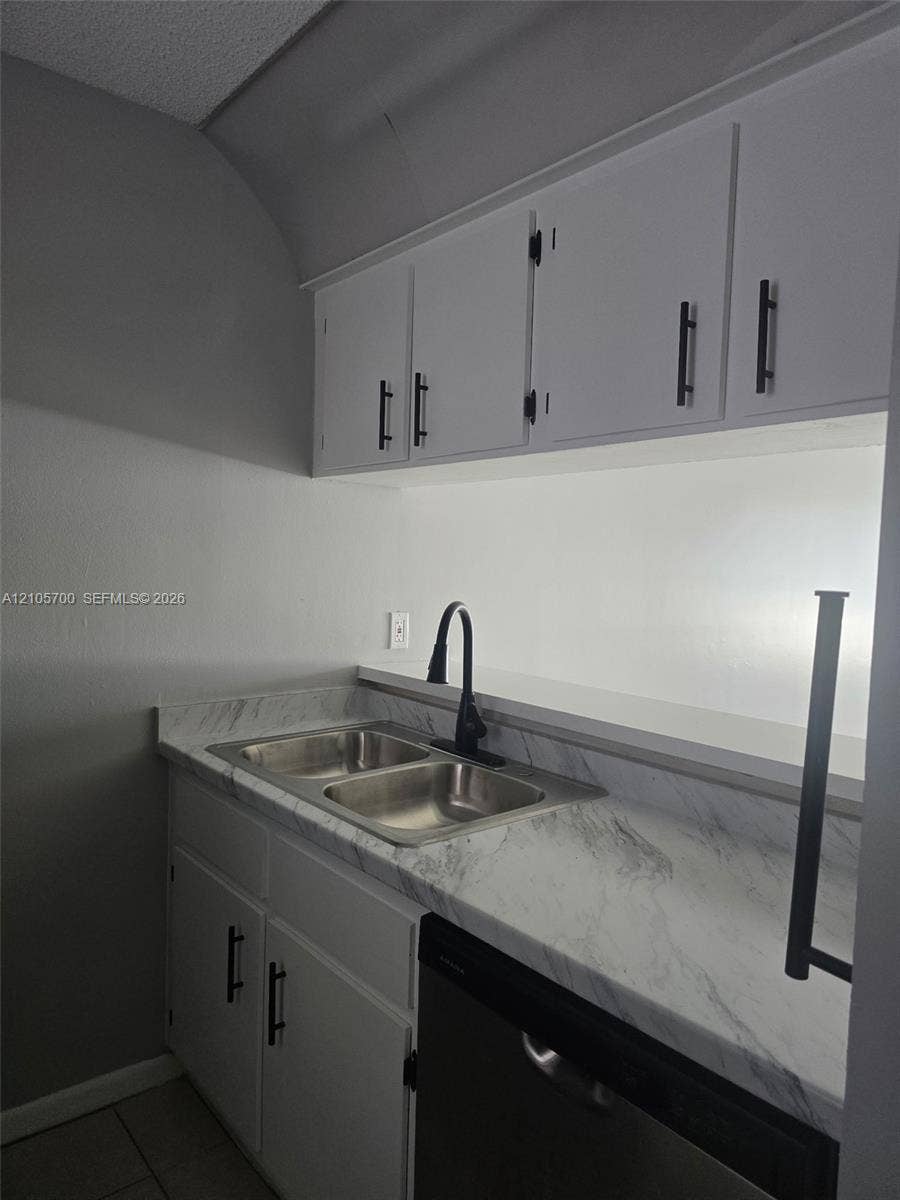 White cabinetry with matte black hardware, stone-finish countertops, stainless steel double-basin sink, and high-arc matte black faucet