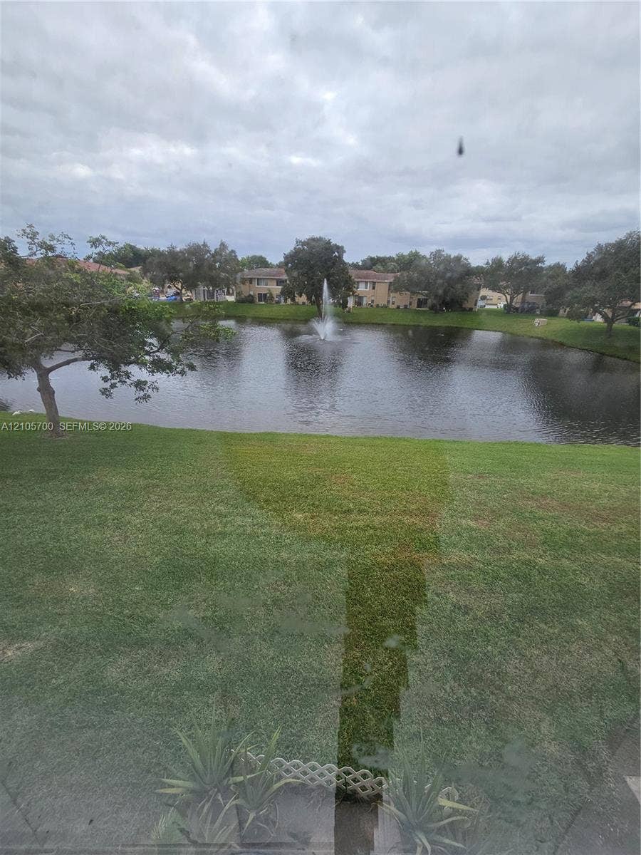 Waterfront lot featuring a pond, a center fountain, and mature trees situated on a grass lawn