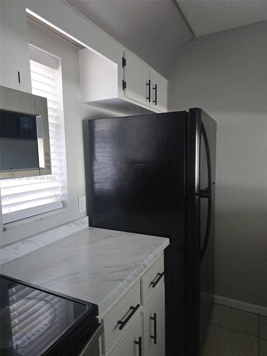 White cabinetry featuring matte black hardware, stone-patterned countertops, and integrated stainless steel and black appliances