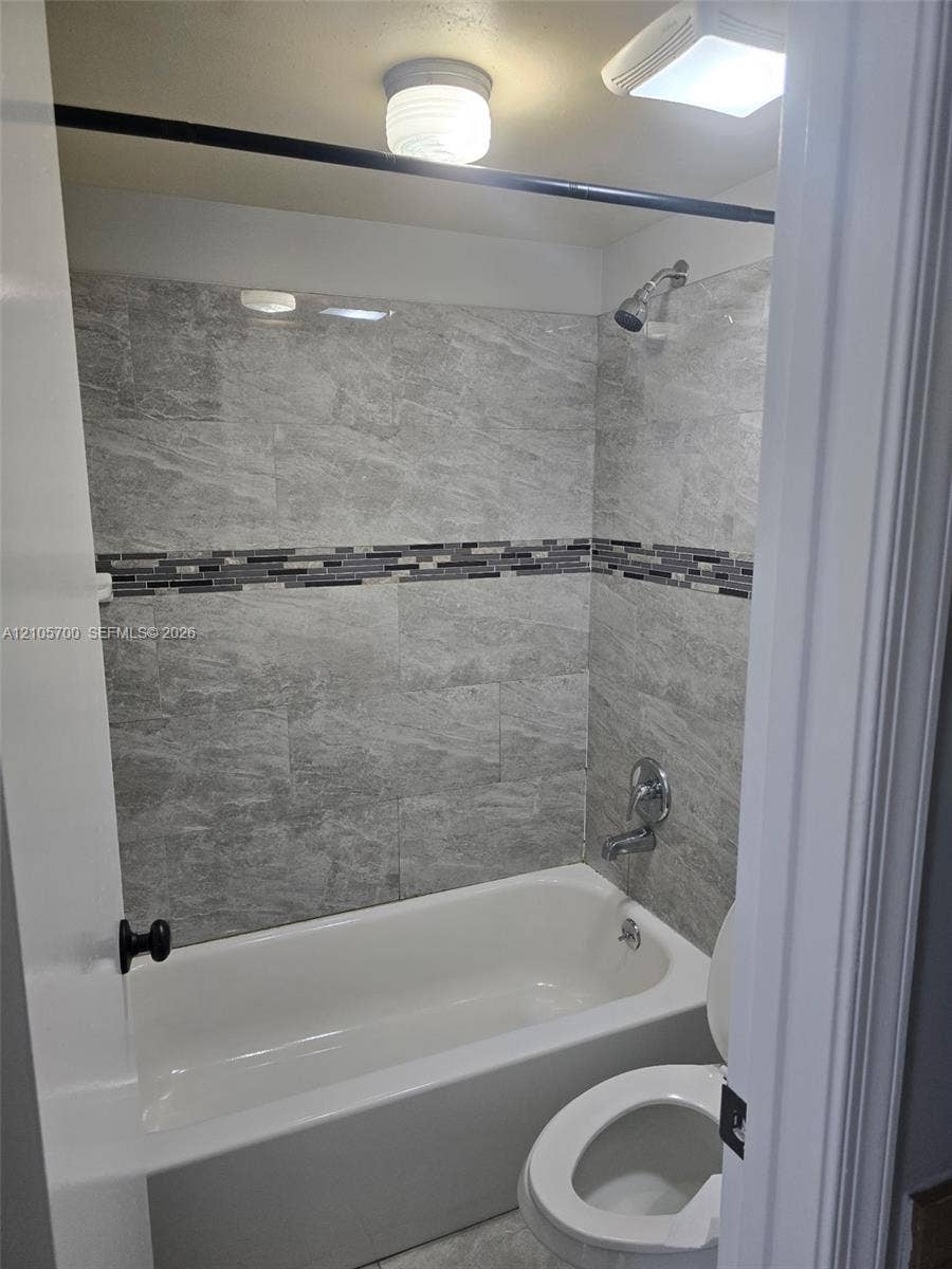 Bathtub surround featuring large-format grey tile, mosaic accent detailing, polished chrome fixtures, and a ceiling-mounted light fixture