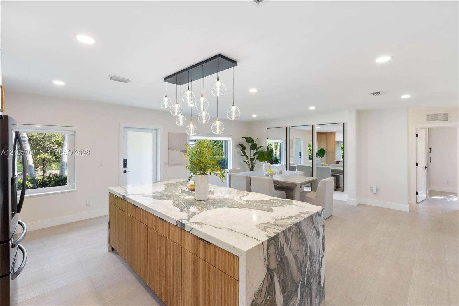 190 NW 102nd Street, Miami Shores, FL 33150 Kitchen island with stone waterfall countertop and natural wood-finish cabinetry, illuminated by a multi-pendant light fixture, complemented by light-toned wood-finish flooring and recessed ceiling lighting