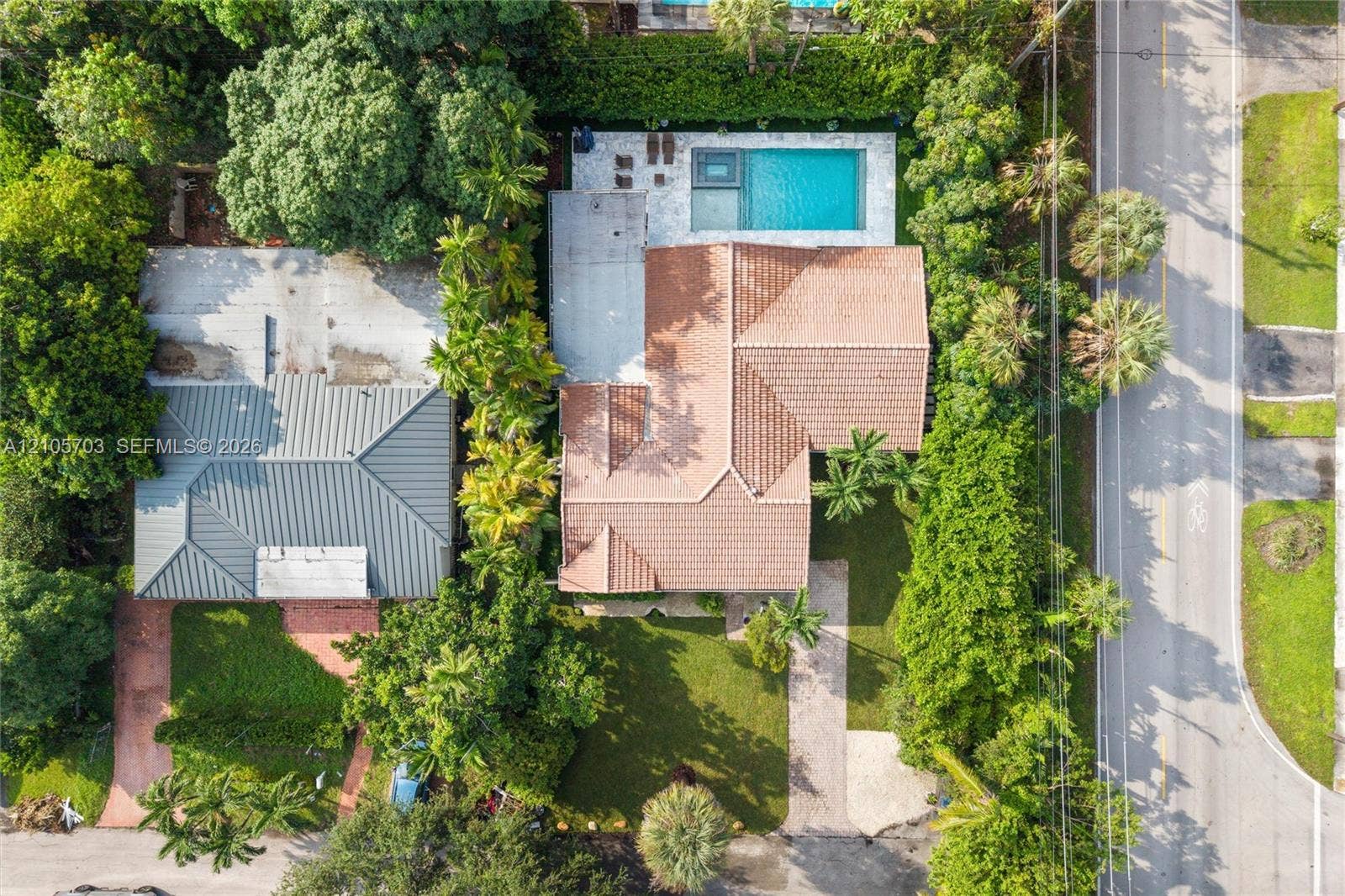 190 NW 102nd Street, Miami Shores, FL 33150 Aerial perspective featuring a tile-roof residence, a rectangular swimming pool, integrated spa, paved patio area, and mature landscaping