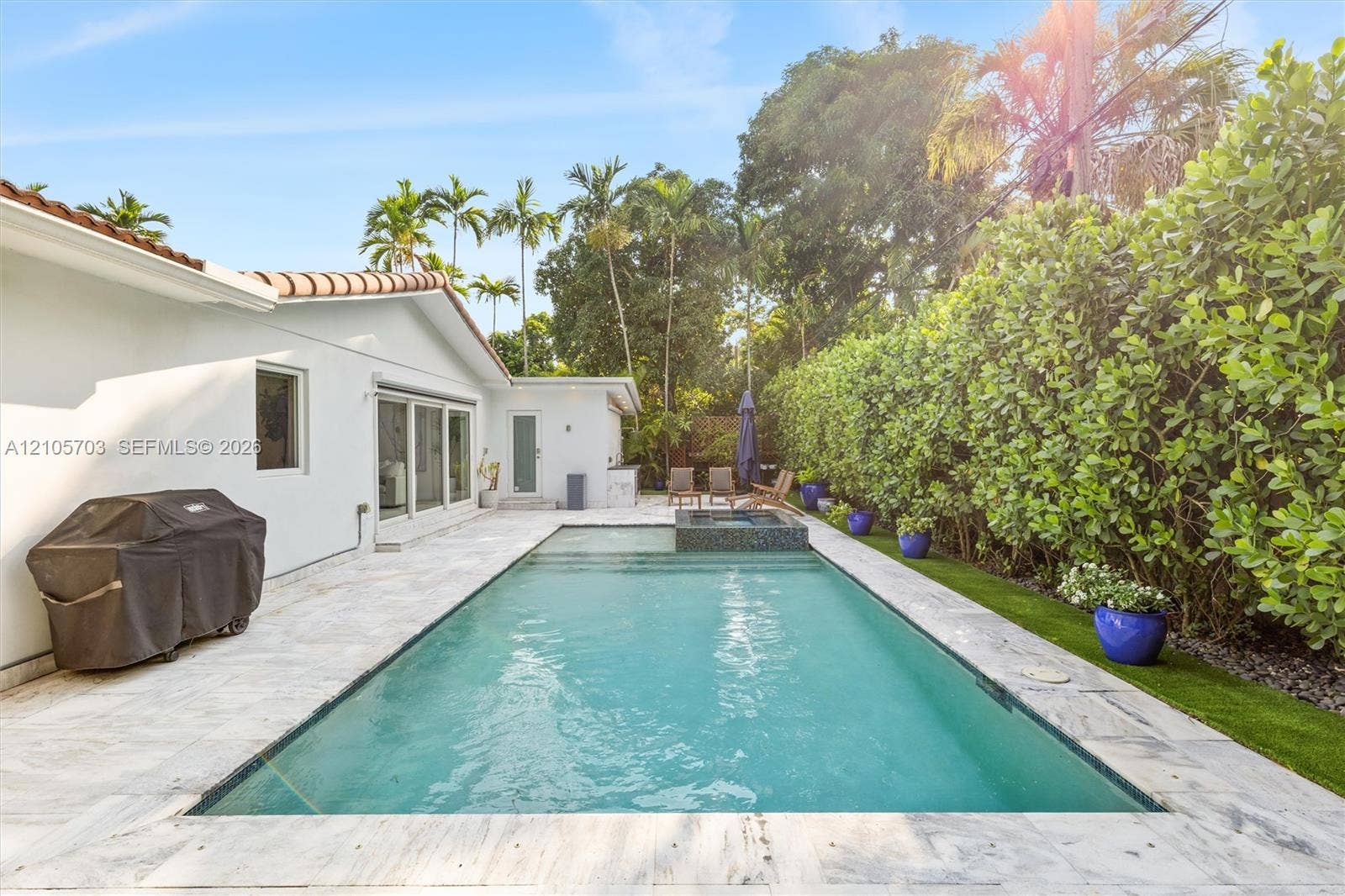 190 NW 102nd Street, Miami Shores, FL 33150 Rear patio featuring an in-ground swimming pool with an integrated spa, stone-finish pool decking, and established privacy landscaping