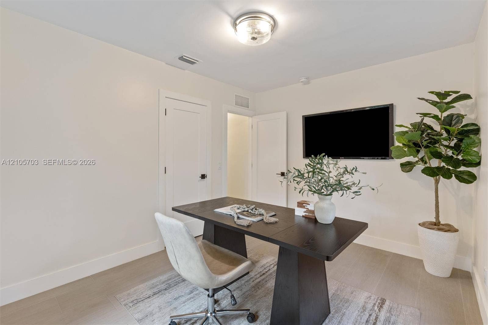 190 NW 102nd Street, Miami Shores, FL 33150 Neutral-toned interior featuring wood-finish flooring, solid-core doors with matte black hardware, and a flush-mount drum ceiling light