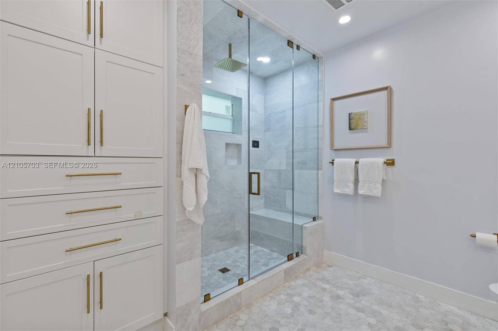 190 NW 102nd Street, Miami Shores, FL 33150 Walk-in steam shower featuring a glass enclosure, built-in stone bench, and rainfall showerhead, accompanied by custom floor-to-ceiling cabinetry with brass-finish hardware