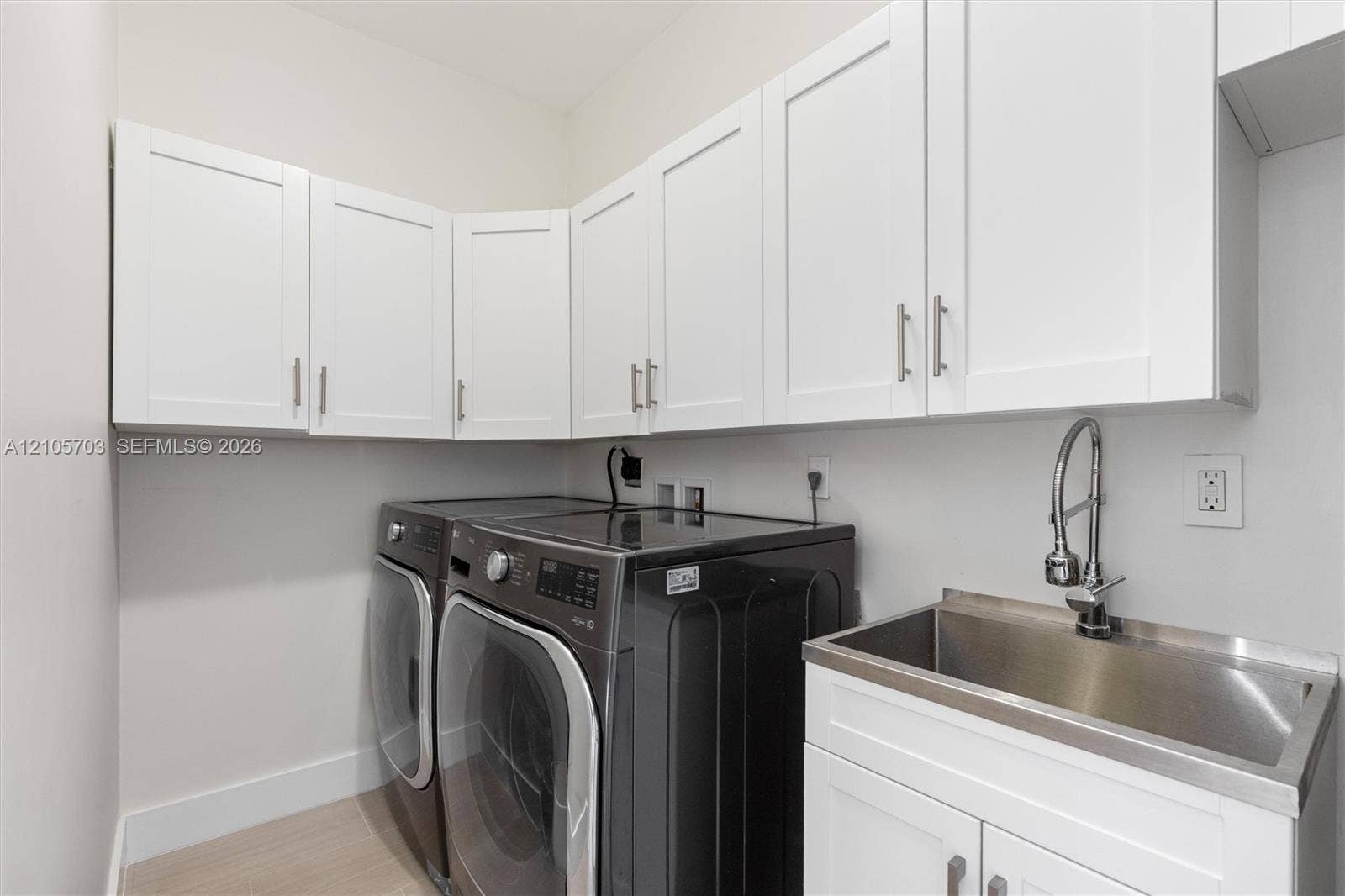 190 NW 102nd Street, Miami Shores, FL 33150 Laundry room featuring white shaker-style wall cabinetry, stainless steel utility sink with a high-arch pull-down faucet, and light-toned flooring