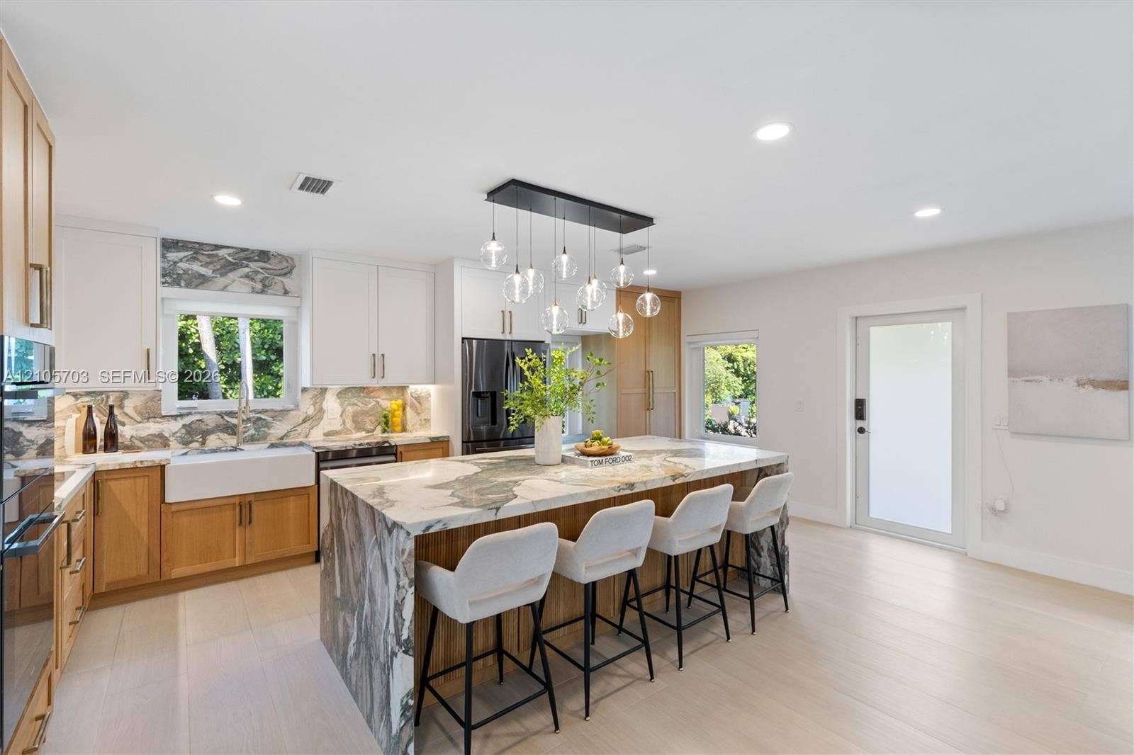 190 NW 102nd Street, Miami Shores, FL 33150 Kitchen featuring a waterfall-edge island with stone surfacing, apron-front farmhouse sink, custom cabinetry with dual-tone finish, built-in stainless steel appliances, and multi-pendant lighting fixture
