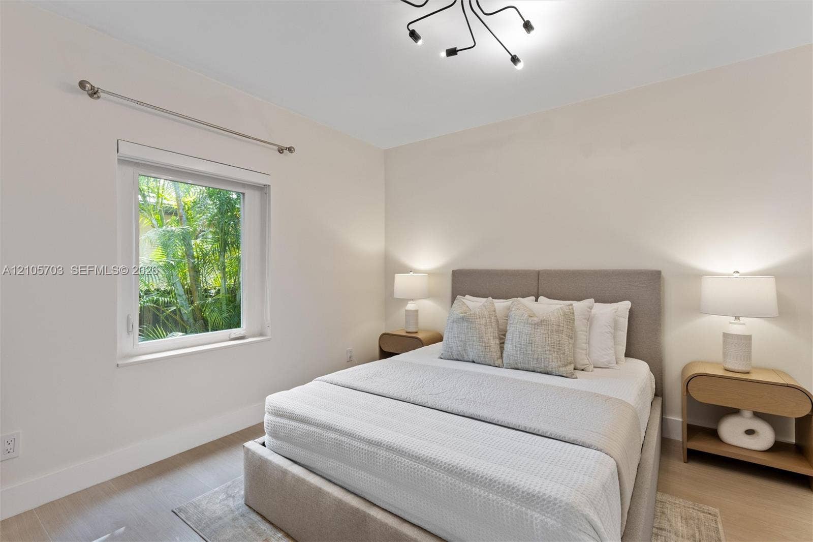 190 NW 102nd Street, Miami Shores, FL 33150 Neutral-toned interior featuring wood-finish flooring, a contemporary multi-arm flush mount light fixture, and a window with exterior greenery