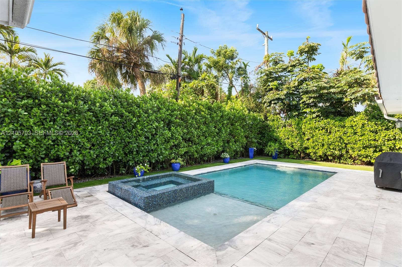 190 NW 102nd Street, Miami Shores, FL 33150 Backyard featuring a swimming pool with a built-in spa, stone patio, and perimeter privacy hedges