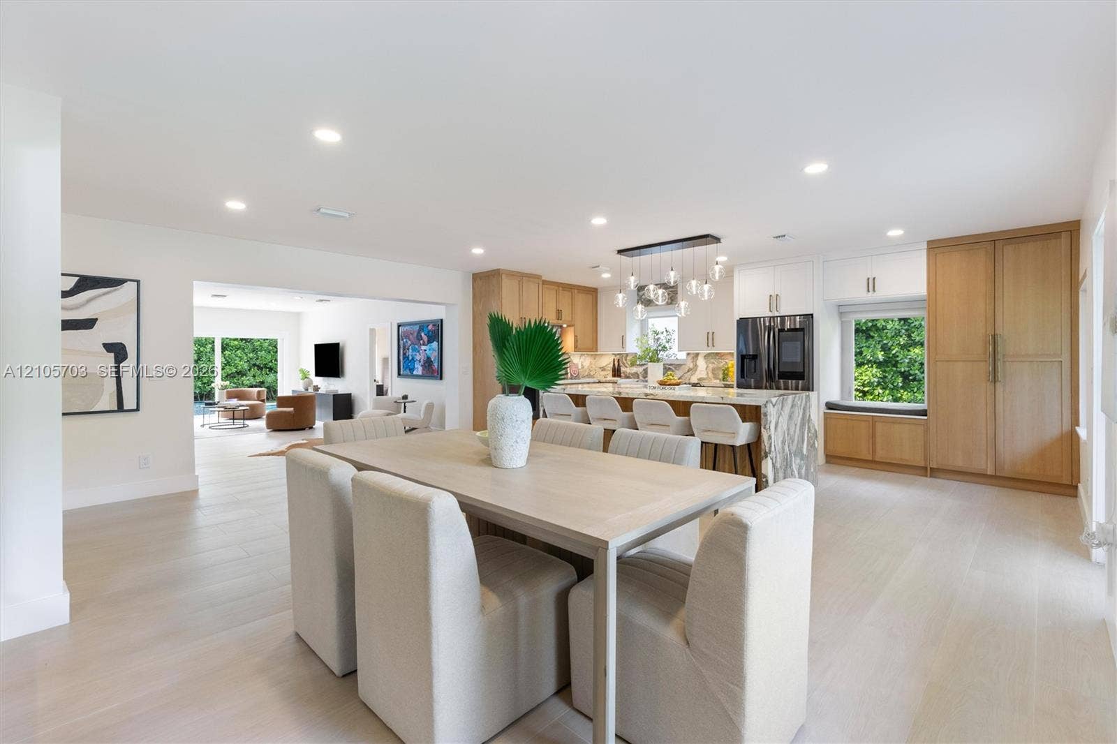 190 NW 102nd Street, Miami Shores, FL 33150 Kitchen and dining area featuring light-tone wood-finish flooring, a waterfall-edge kitchen island, integrated cabinetry, recessed lighting, and a linear multi-pendant light fixture