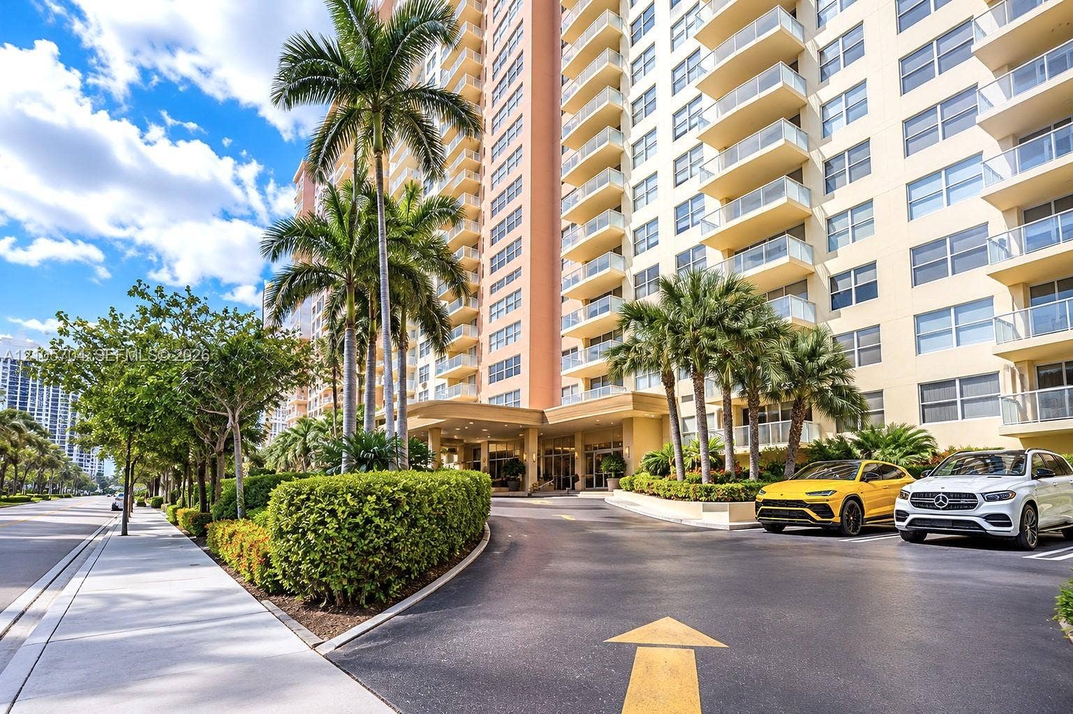 251 174th Street, #212, Sunny Isles Beach, Sunny Isles Beach, FL 33160 High-rise building exterior featuring a covered porte-cochere, glass-railed private balconies, mature palm trees, and manicured shrubbery