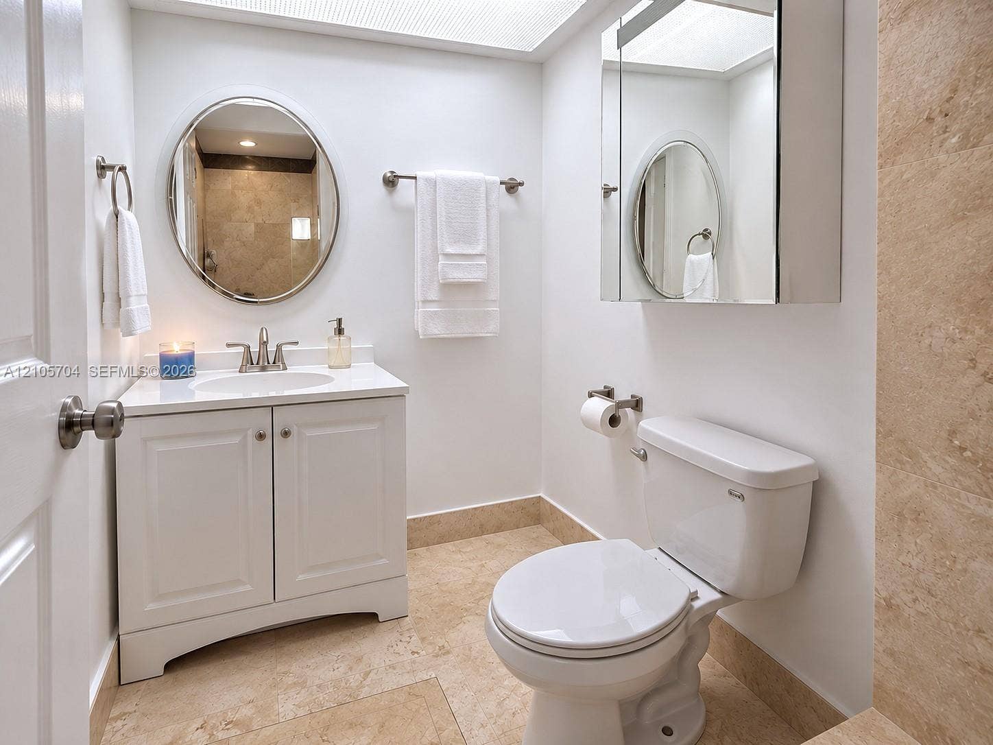 251 174th Street, #212, Sunny Isles Beach, Sunny Isles Beach, FL 33160 White vanity with a stone countertop, oval wall-mounted mirror, inset medicine cabinet, and light-toned stone tile flooring